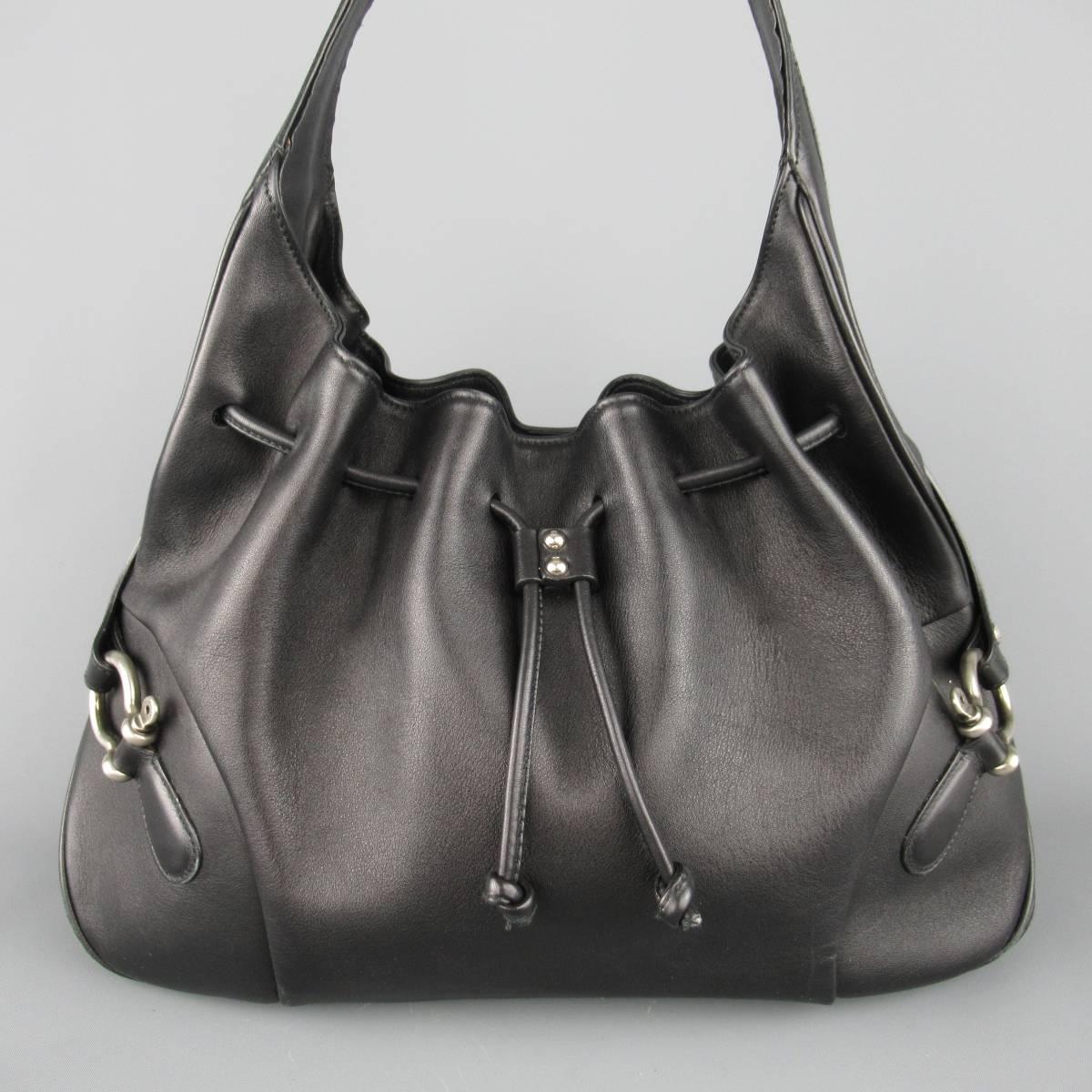 BURBERRY LONDON hobo shoulder bag comes in smooth black leather and features symmetrical harness side details with antiqued silver tone hardware, leather shoulder strap, and drawstring top with magnetic closure. Wear on lining and studs loose on