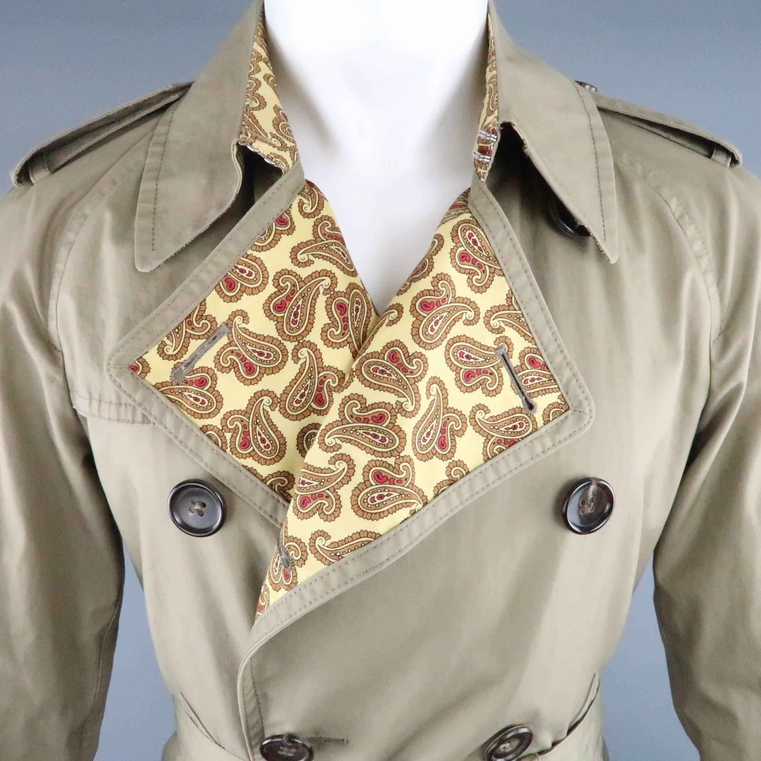 JUNYA WATANABE MAN trench coat comes in dark khaki cotton with raglan sleeves, storm flap, hook eye collar, belted waist and cuffs, epaulets, and yellow and red paisley print lining. Made in Japan.
 
Good Pre-Owned Condition.
Marked: S  AD 2008
