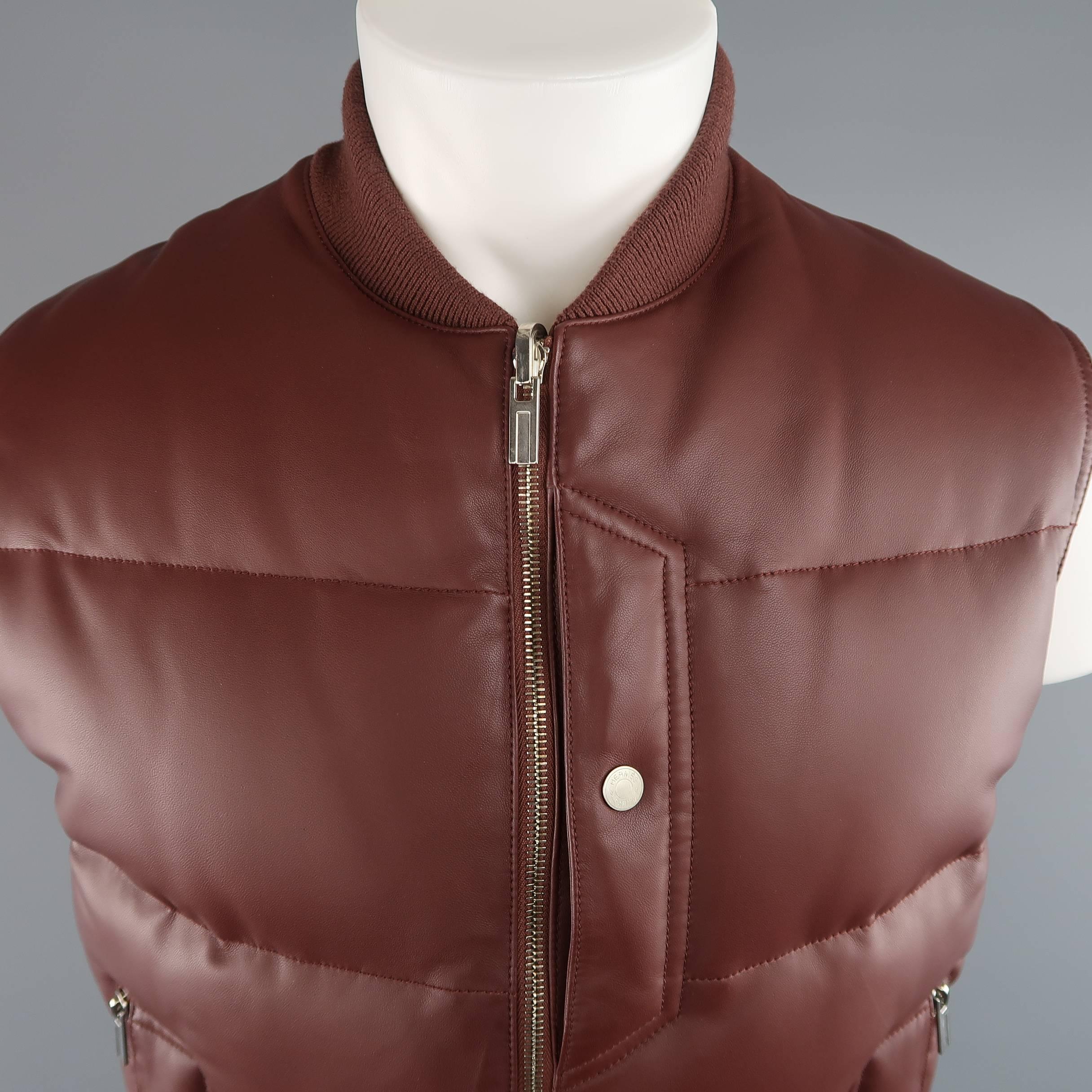 HERMES down filled puff vest comes in a rich light burgundy brown quilted lambskin leather and features a knit baseball collar, silver tone double zip front, triple snap and zip pockets, underarm grommets, and reverse nylon option. Made in France.
