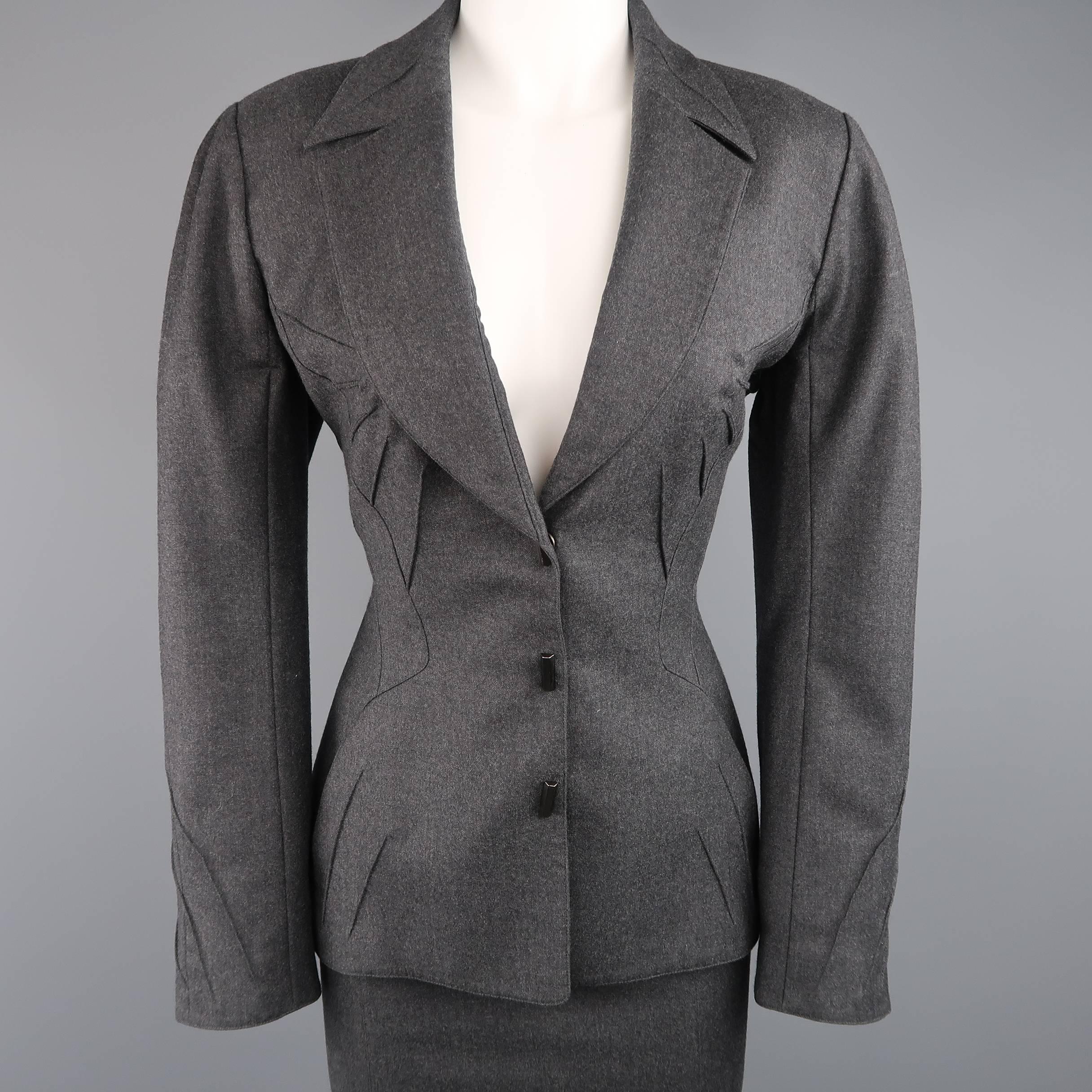 This gorgeous early 1990's THIERRY MUGLER suit comes in a soft dark heather gray wool and includes a cinched waist, cropped jacket with unique piping details throughout, signature downward point lapel, and triple snap studded closure with matching