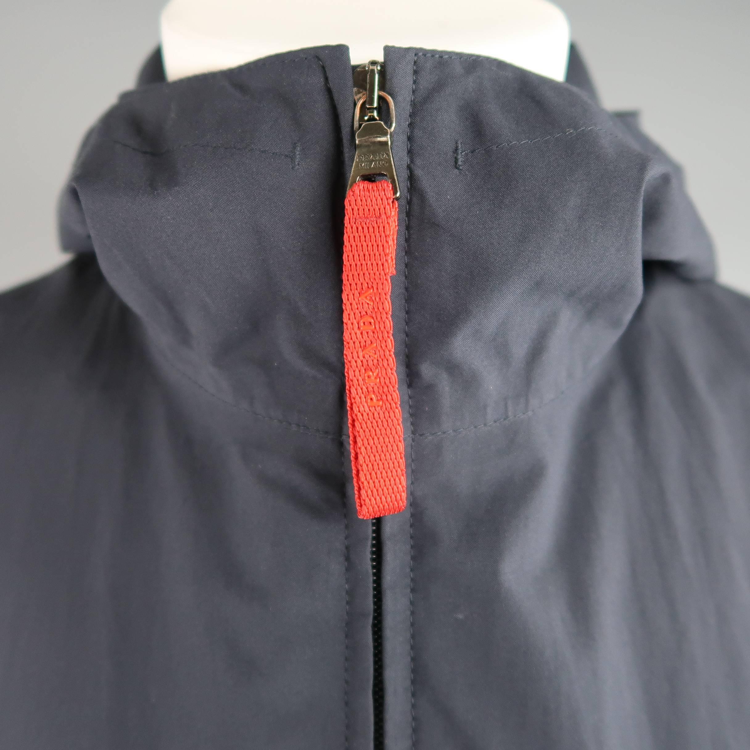 Classic PRADA overcoat comes in a light weight navy blue nylon and features a high neck with hood, double zip with red logo tab, frontal zip pockets, black GORE-TEX liner with extended stretch cuffs, and back zip pockets. Made in Italy.
 
Good