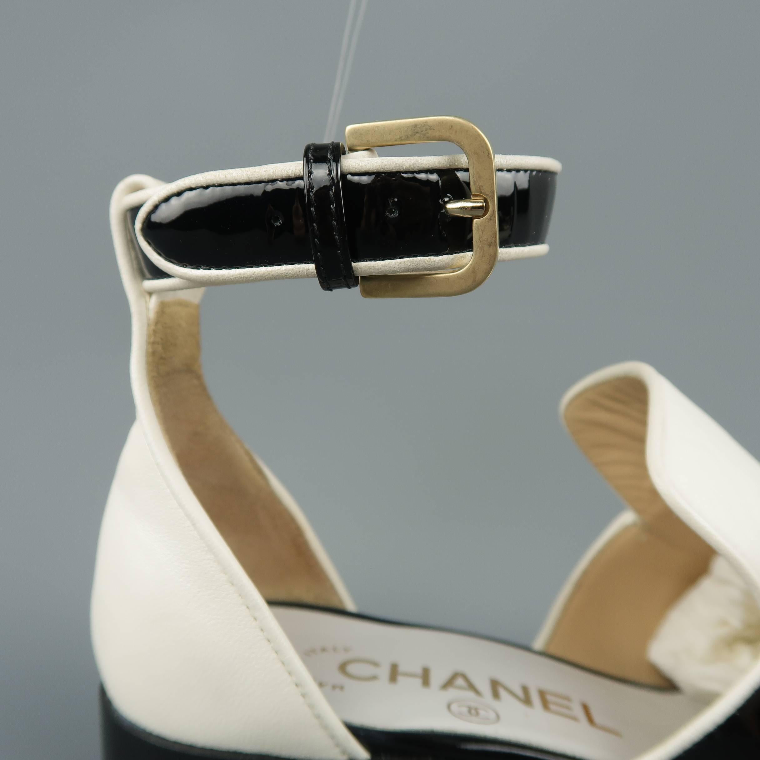 CHANEL loafers come in cream smooth leather and feature a split toe with black patent leather accent, light gold tone metal embossed coin embellishment, open mid section, low heel, and ankle strap. Sole added. Very minor wear. Made in Italy.
