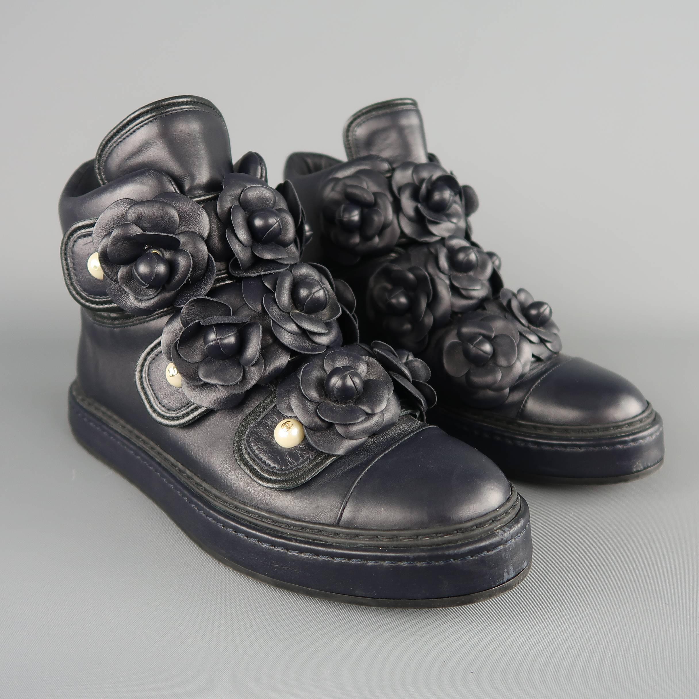 Chanel high top sneakers come in navy blue leather with three velcro straps embellished with leather camellia flowers. Wear throughout. CC logo missing from top pearl on both shoes. As-is.  Made in Italy.  Good Pre-Owned Condition.
Marked: IT 37
