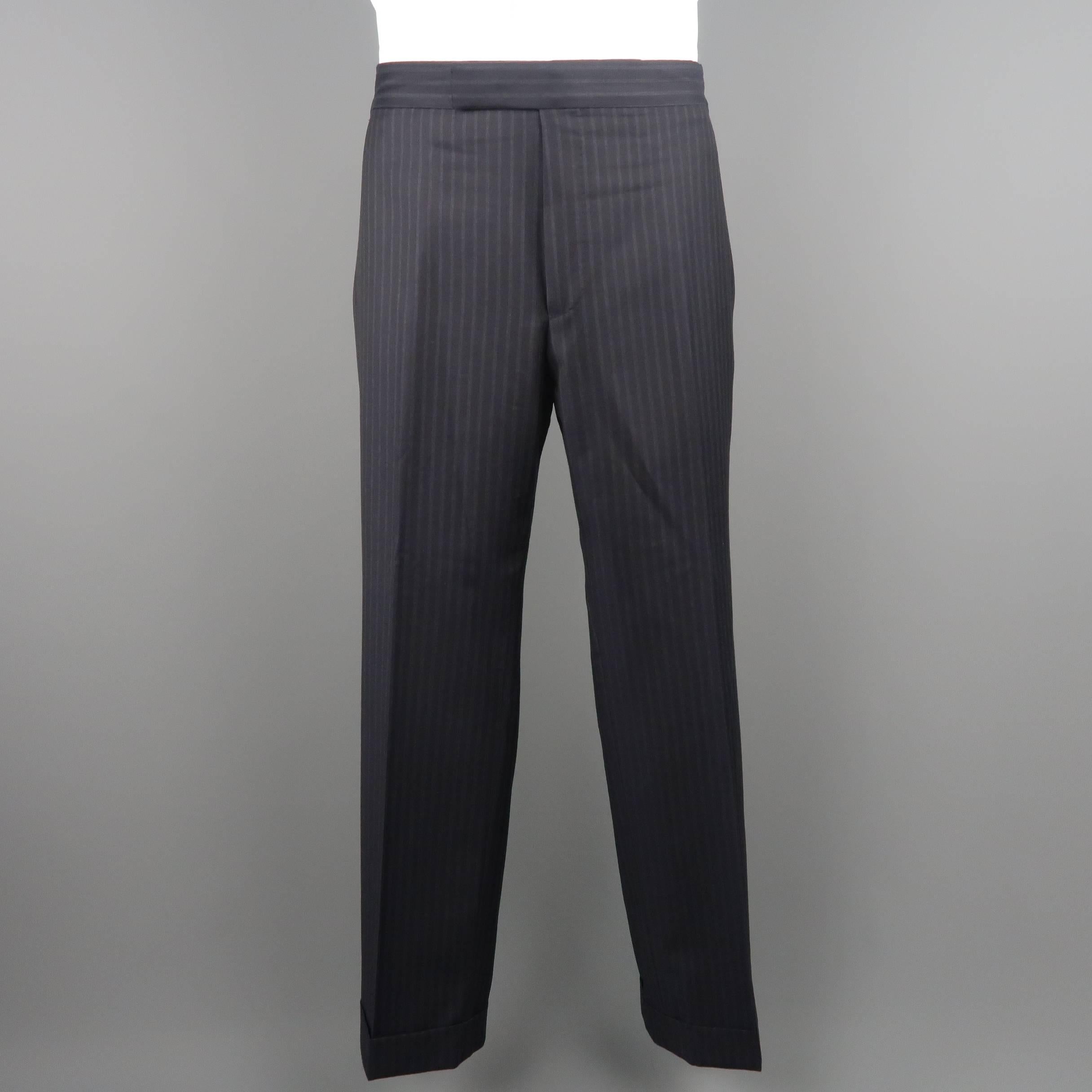 Two piece Tom Ford suit comes in black pinstriped wool twill and includes a single breasted, two button sport coat with notch lapel, triple flap pockets, and functional button cuffs with matching flat front, cuffed dress pants.  Made in Italy.
