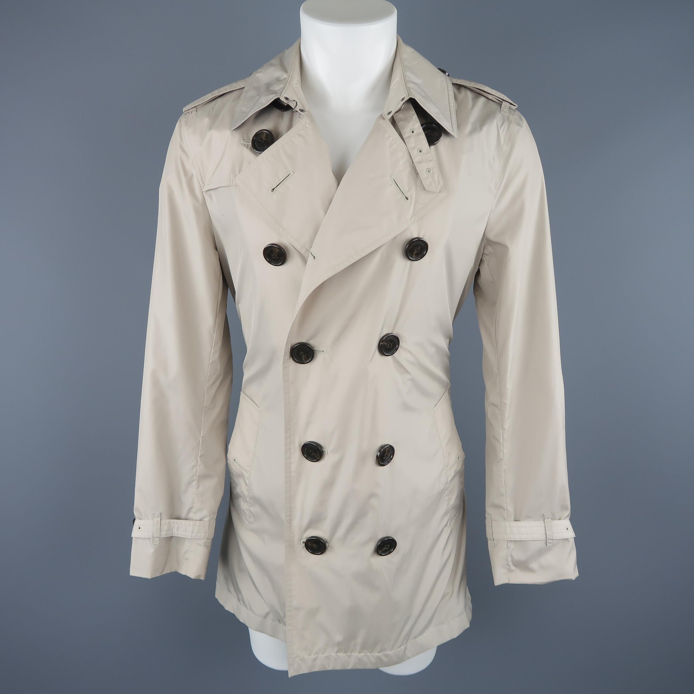 Burberry London trench coat comes in light khaki windbreaker material with a plaid lined pointed collar, storm flap, double breasted button up closure, belted waist, epaulets, and belted cuffs. Stains shown in detail shots .As-is. With garment bag.
