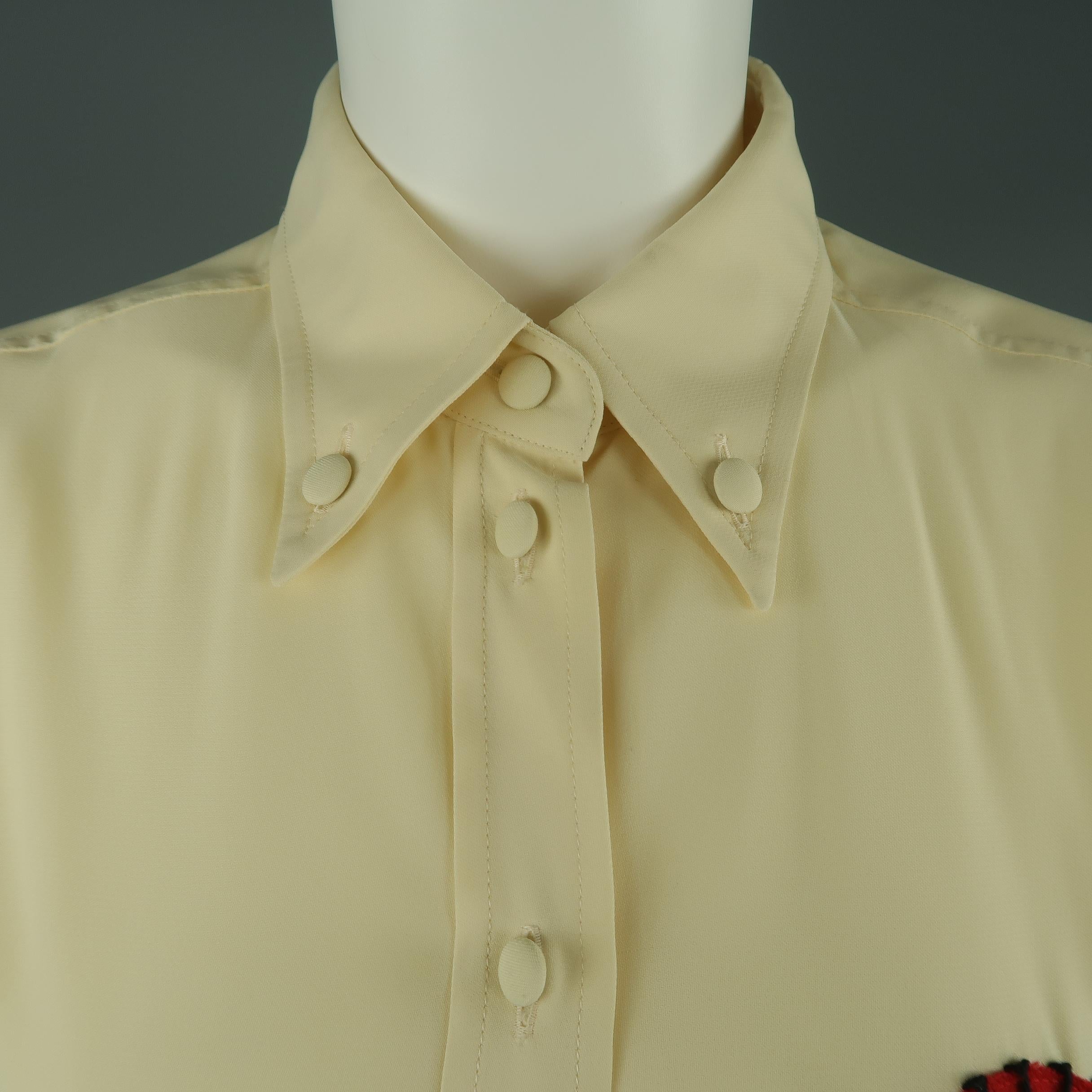 Moschino Couture blouse comes in a creamy beige crepe with fabric buttons, pointed button down collar, and red stitched heart applique. Made in Italy.
 
Excellent Pre-Owned Condition.
Marked: 12
 
Measurements:
 
Shoulder: 17 in.
Bust: 44