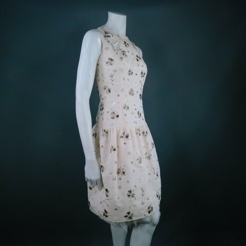 Stunning sleeveless cocktail dress by OSCAR DE LA RENTA. This show stopping number in off white silk features a high neckline, fitted bodice beaded in a snow flake floral print, and gathered drop waist skirt finished in luxurious white rooster
