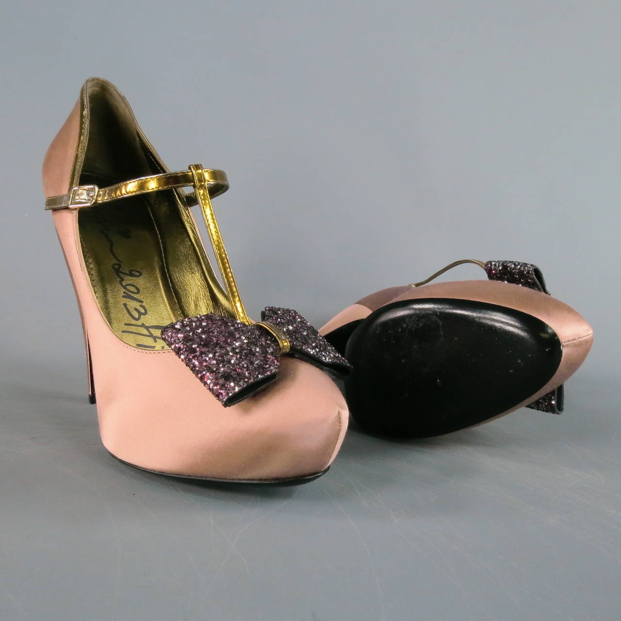 Angular platform pumps by LANVIN. A fabulous style featuring a concealed platform and thick stiletto heel covered in dusty rose pink satin, metallic gold leather T strap with matching piping, and glitter bow embellishment. Fun and girly yet high