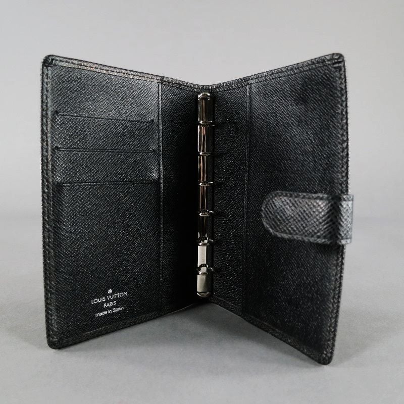 This Louis Vuitton Black Taiga Leather Small Agenda PM Planner LV Organizer features
hidden snap closure. Leather lining. Six ring binder & pen holder slot. On its right side, there's a side slot for papers and a slot for cards. On the left,