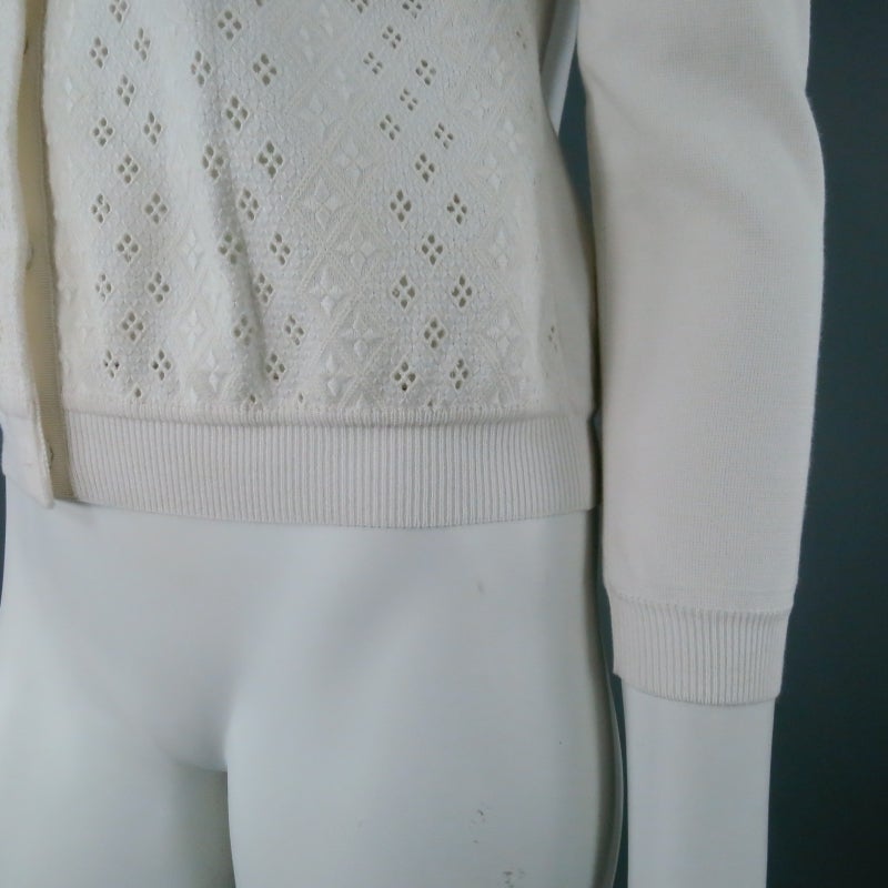 Lovely cream knit cardigan by GIAMBATTISTA VALLI. A retro style with modern details, this piece features a diamond lace front panel with covered snap closure, finished in ribbon. A great weight for spring outer wear. Made in Italy.

Excellent