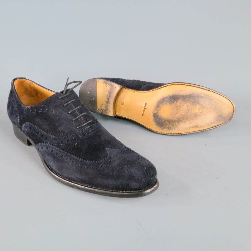 KITON Lace Up Shoe consists of a suede material in a navy color tone. Designed in a  wingtip brogue style, perforated detailing can be seen throughout body of shoe with tone-on-tone stitching. Contrast black leather sole with textured appearance.