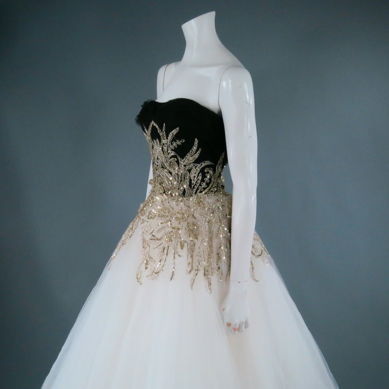 Stunning two tone evening gown by MARCHESA. In a classic silhouette, this creation comes in a black layered tulle bodice with white tulle skirt and features beautiful metallic gold vine embroidery with sequin floral applique along the waistline.
