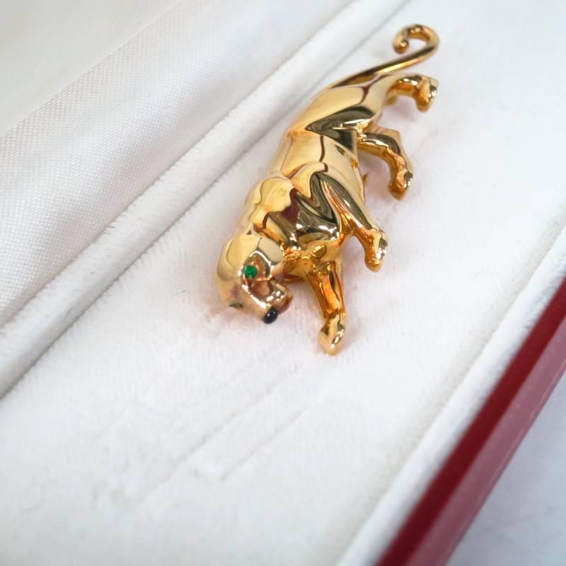 Fabulous vintage pin by CARTIER. This ultra rare style comes in the iconic signature Jaguar Panthere motif in solid 18K yellow gold and features two green emerald eyes, a black onyx nose, and a double point pin back with fastener. This piece comes