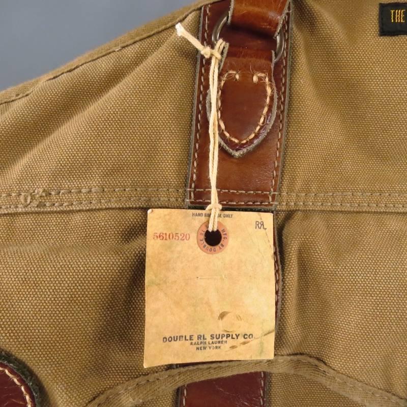 RRL by Ralph Lauren Garment Bag consists of canvas material in a khaki brown color tone. Designed with a leather handles in a tan color tone, tone-on-tone stitching can be seen throughout bag, 3 leather buckles are featured on both sides with