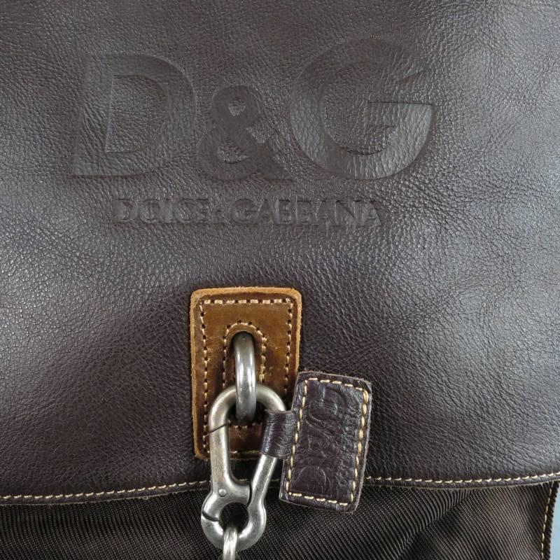 This messenger bag by D&G comes in a brown canvas and leather mix and features a flap with embossed logo that closes with a silver tone chain with 