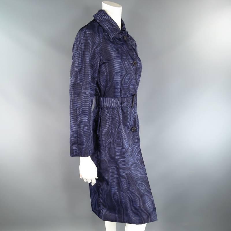 This classic twist PRADA trench coat comes in a navy blue Maore glitch stripe print nylon and features a pointed collar with storm flap, cropped raglan sleeve, single breasted button up closure, and matching belt with black leather buckle. Made in