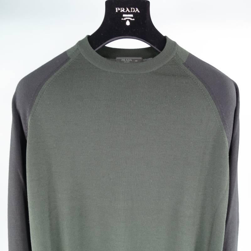Prada Pullover consists of merino wool material in a green and black color tone. Designed with a raglan chest pattern, color blocked appearance with black sleeves, charcoal cuffs and green body. Crew-neck detail, ribbed cuffs, light weight fabric