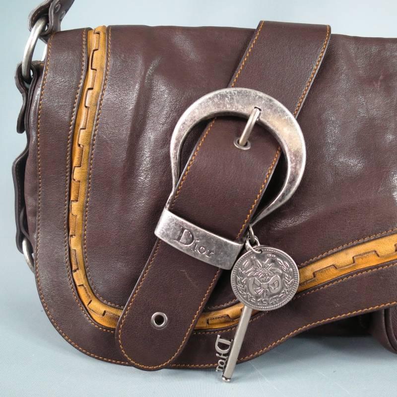 Iconic brown leather Gaucho shoulder bag by DIOR. This signature style comes in smooth brown leather with tan stitching and features a saddle flap with tan leather piping, belt detail with silver tone buckle embellished with 