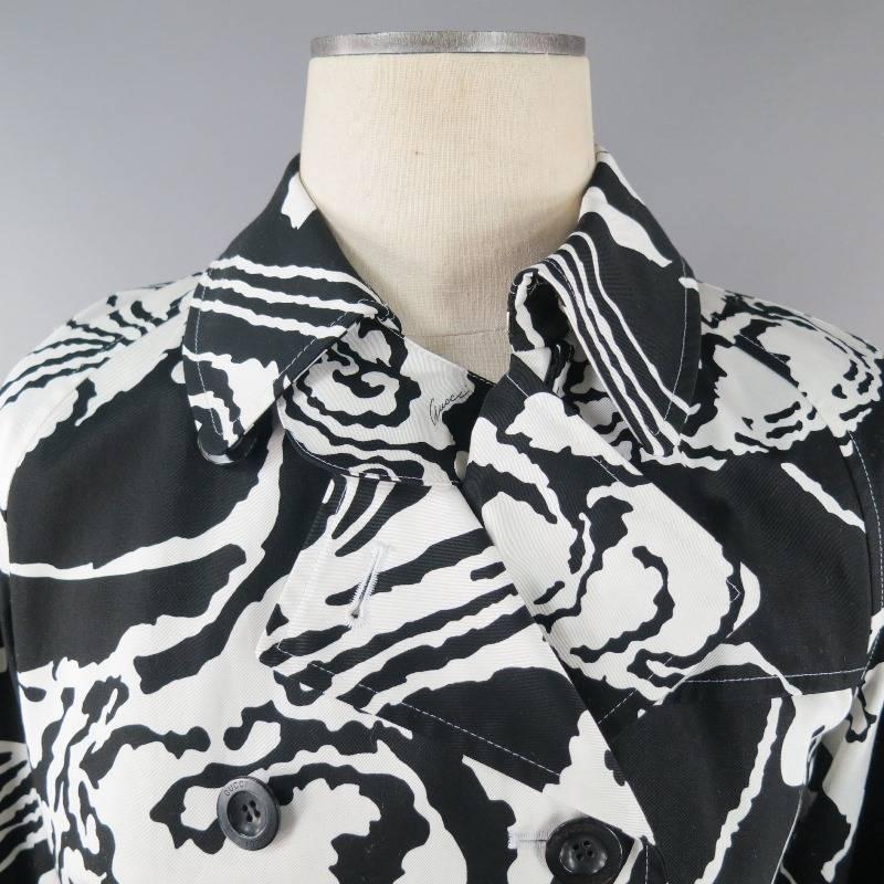 GUCCI trenchcoat in black and white, medium weight cotton with some stiffness; comes in an oversized floral pattern with 'Gucci' printed subtly throughout.  Dual pockets with GG hardware on left side.  Adjustable sleeve loops and belt at waist; both