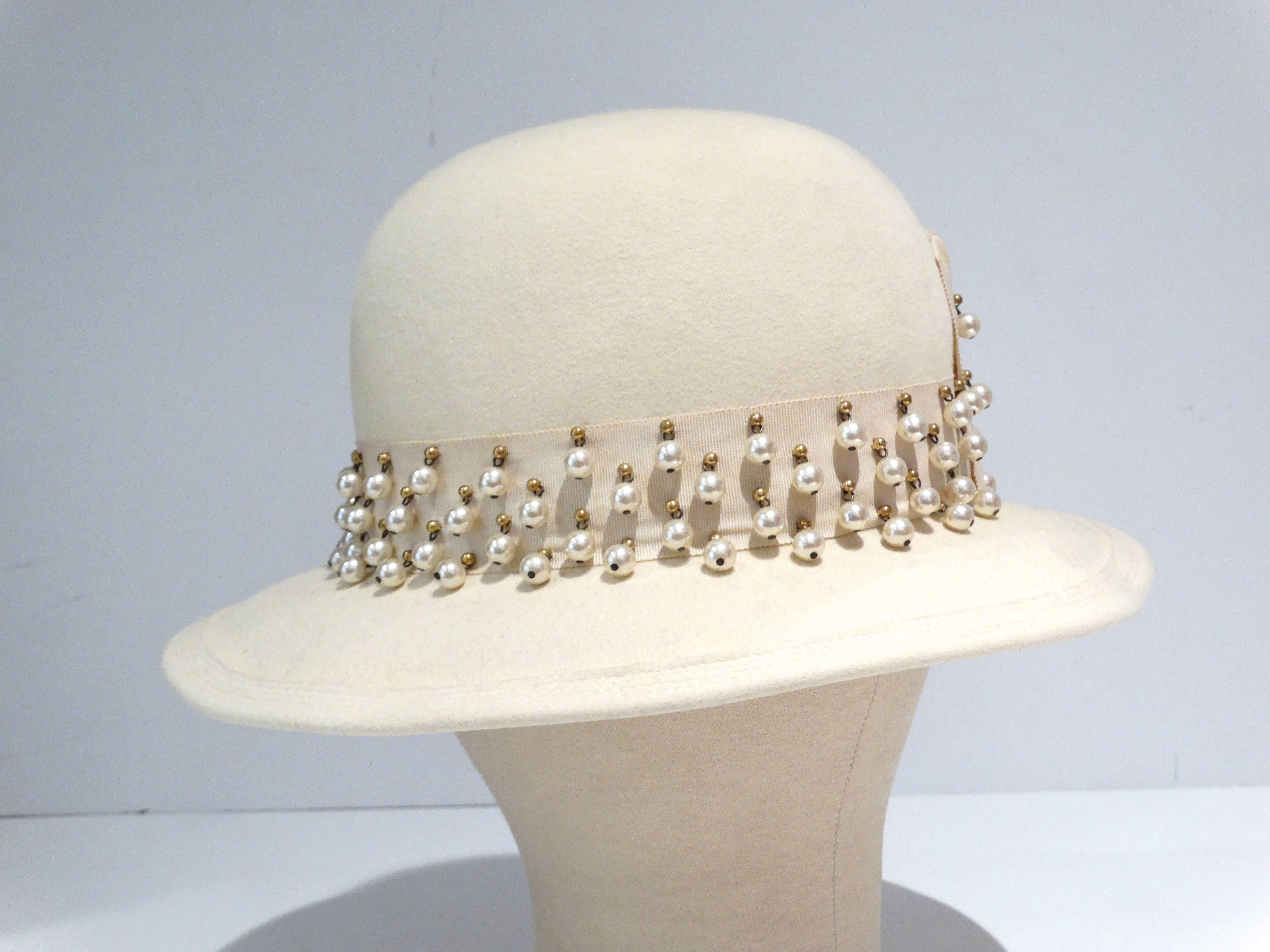 1970s YVES SAINT LAURENT derby style hat made of ivory wool velour.  The high crown is circled w/a grosgrain ribbon band trimmed w/brass studs and dangling simulated pearls.  Channel stitching around the edge of the 2 1/4