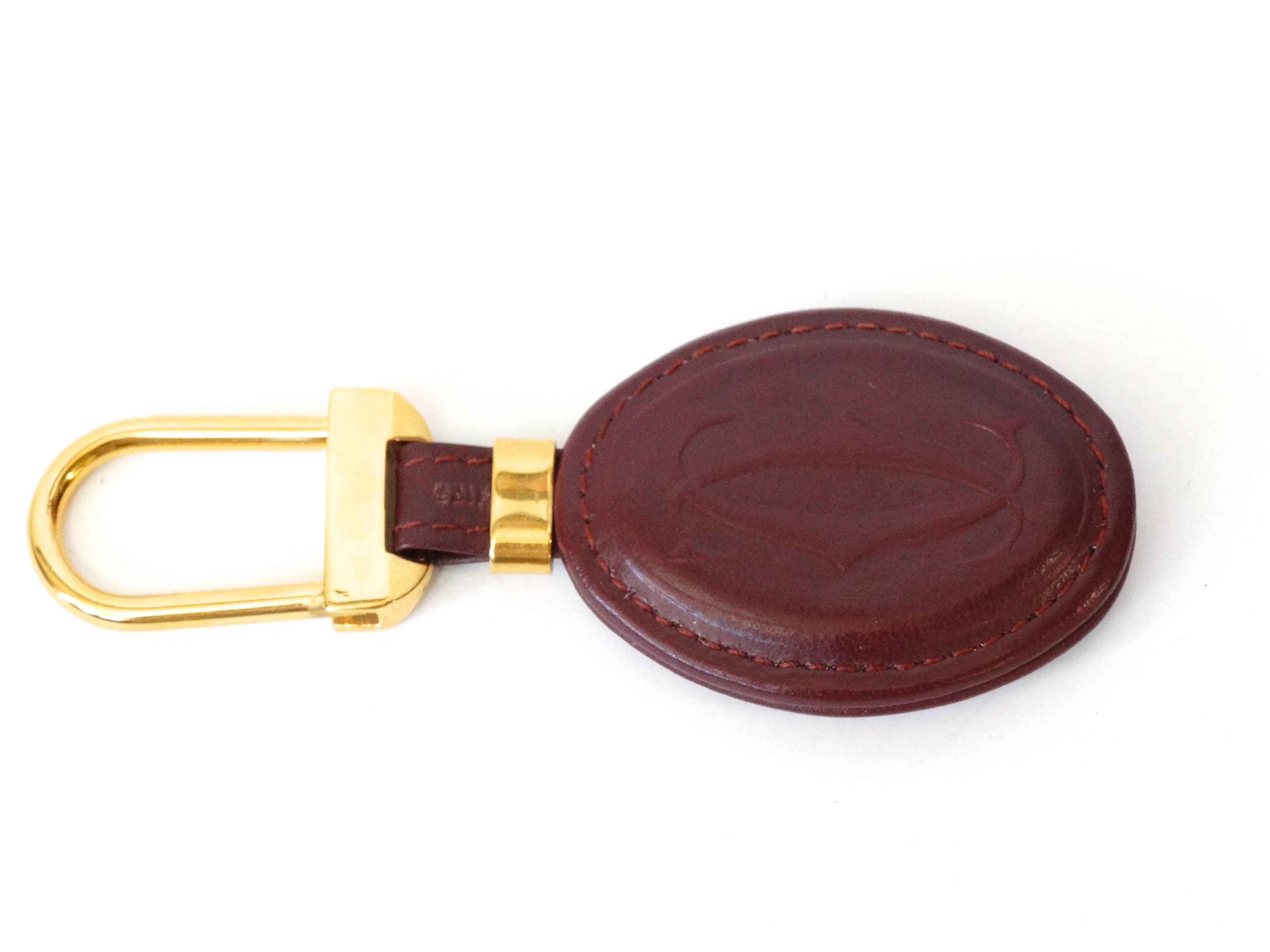 This stylish keychain features an oval pad of burgundy leather embossed with the Cartier logo with a 18kt plated brass ring. This is a marvelous keychain that is as practical as it is chic. Comes with original box

Size: Length: 2