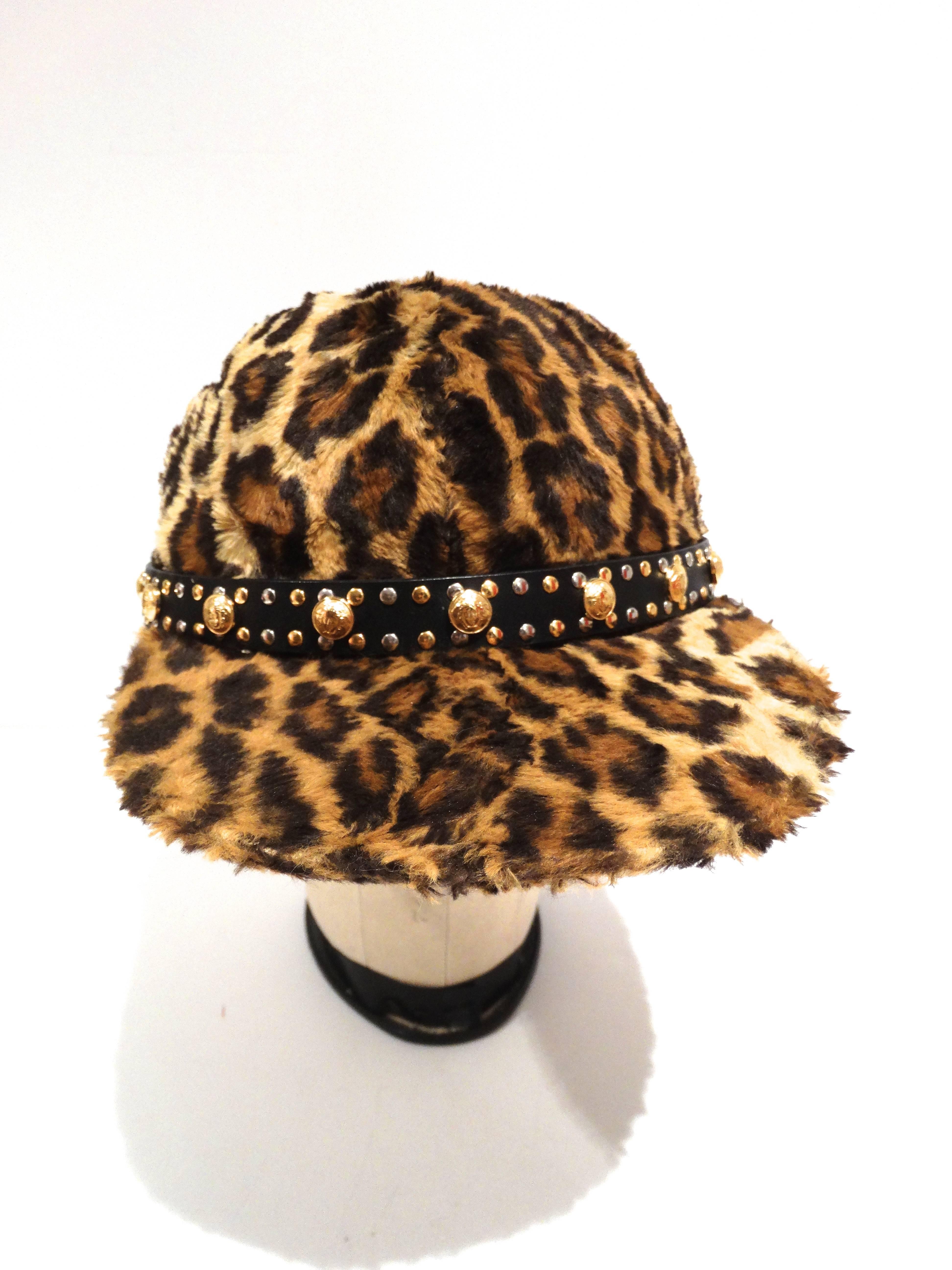 Véritable pièce de collection, cette casquette de baseball Versace de 1992 est recouverte de fausse fourrure léopard, d'une ceinture en cuir avec des têtes de méduses dorées et des clous argentés et dorés. Cette casquette est munie d'une boucle en