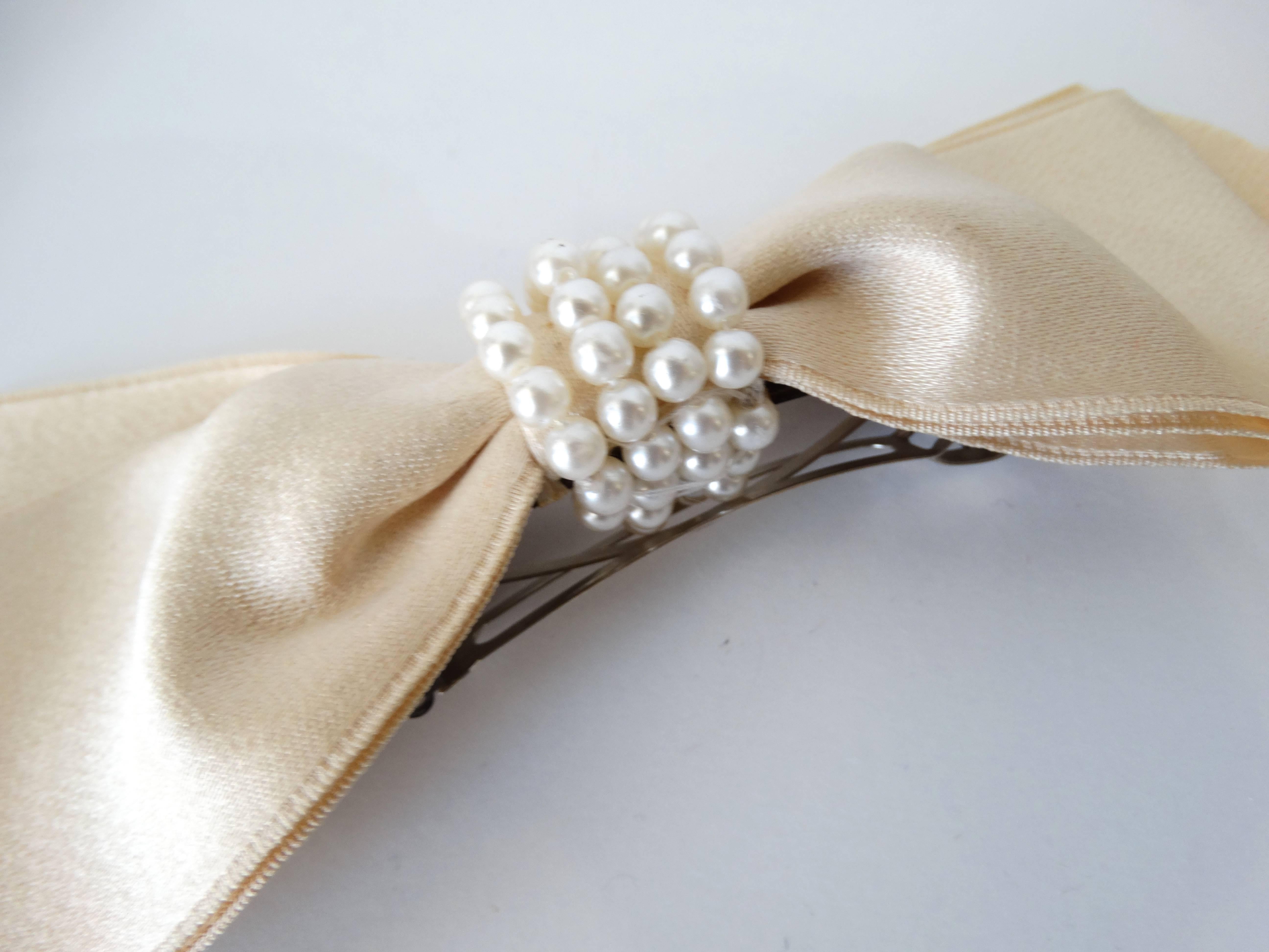Classic 1980's Chanel Cream Satin Hair Bow with 4 strand Pearl details in the center (the bow is wired to maintain its curved shape) with attached barrette. Sophisticated and demure. 
Chanel signature plate attached. 
Measurements: 
7 inches by 2