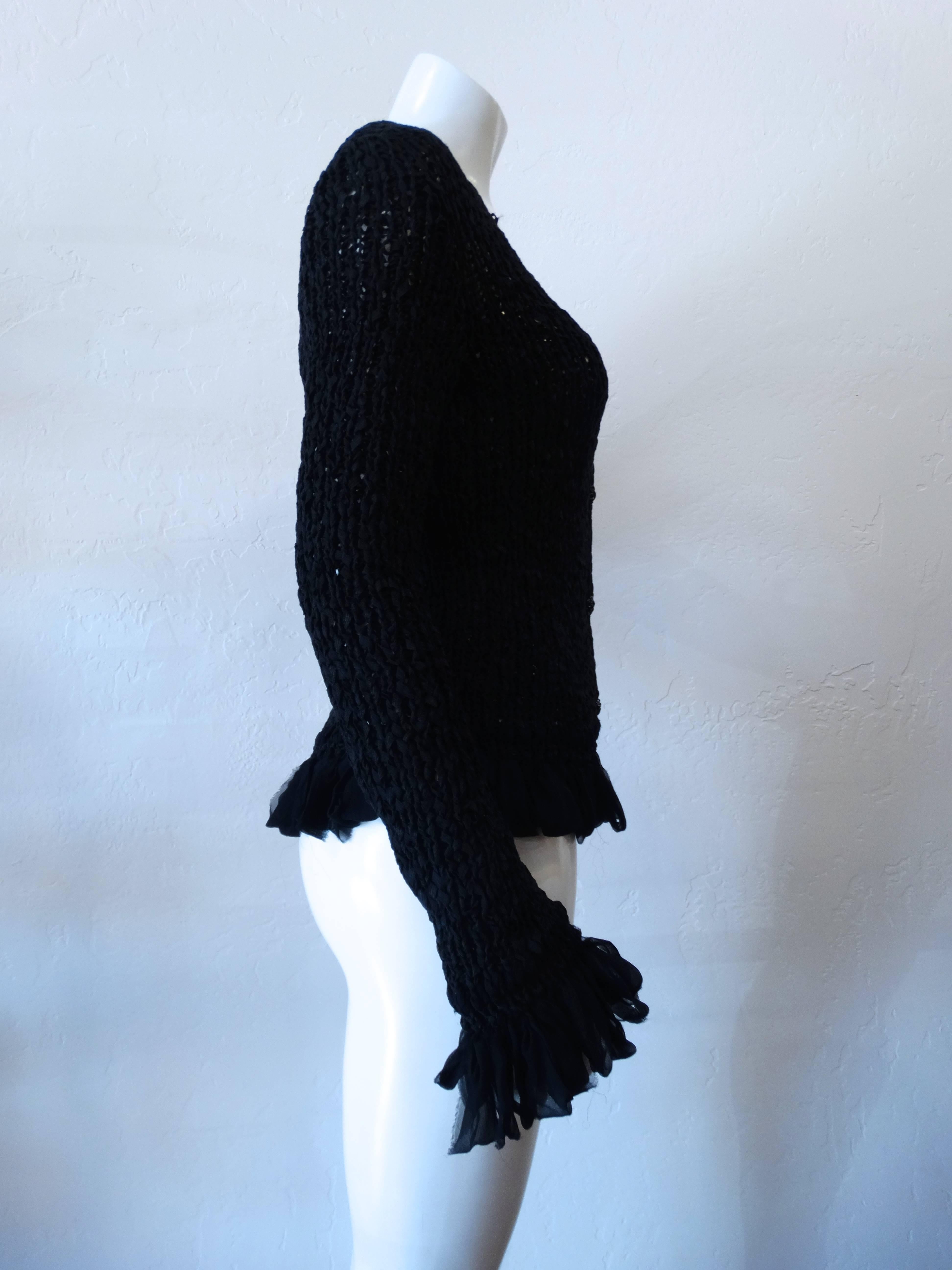 Chanel button up crochet sweater from the 2002 Cruise collection. Loose cotton, silk and nylon blend crochet accented with sheer ruffles at the sleeves and hem. Adorable black Camilla floral button closures up the front. Marked a size 42. 

Sleeve