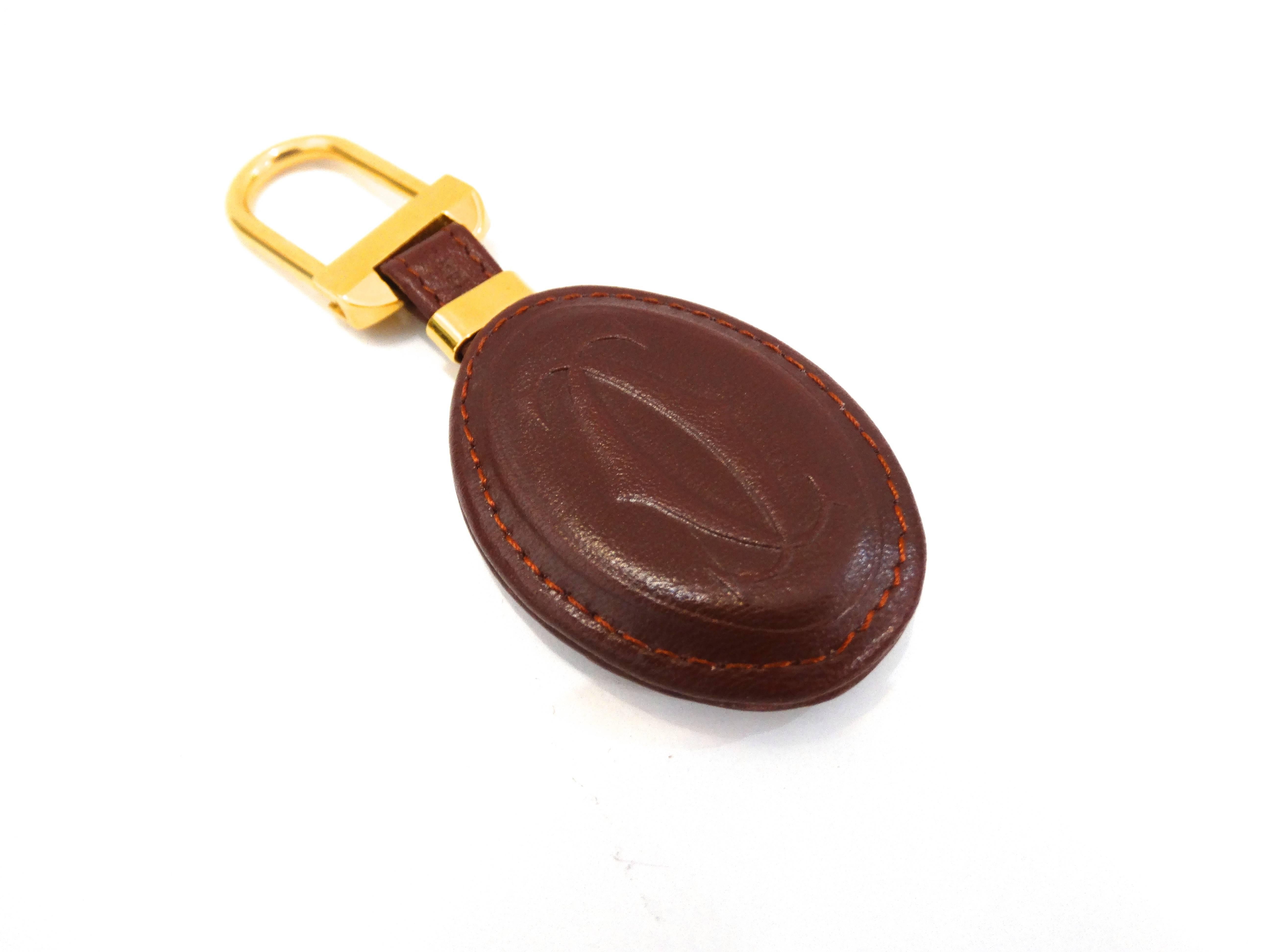 This stylish keychain features an oval pad of burgundy leather embossed with the Cartier logo with a 18kt plated brass ring. This is a marvelous keychain that is as practical as it is chic. Comes with original box

Size: Length: 2