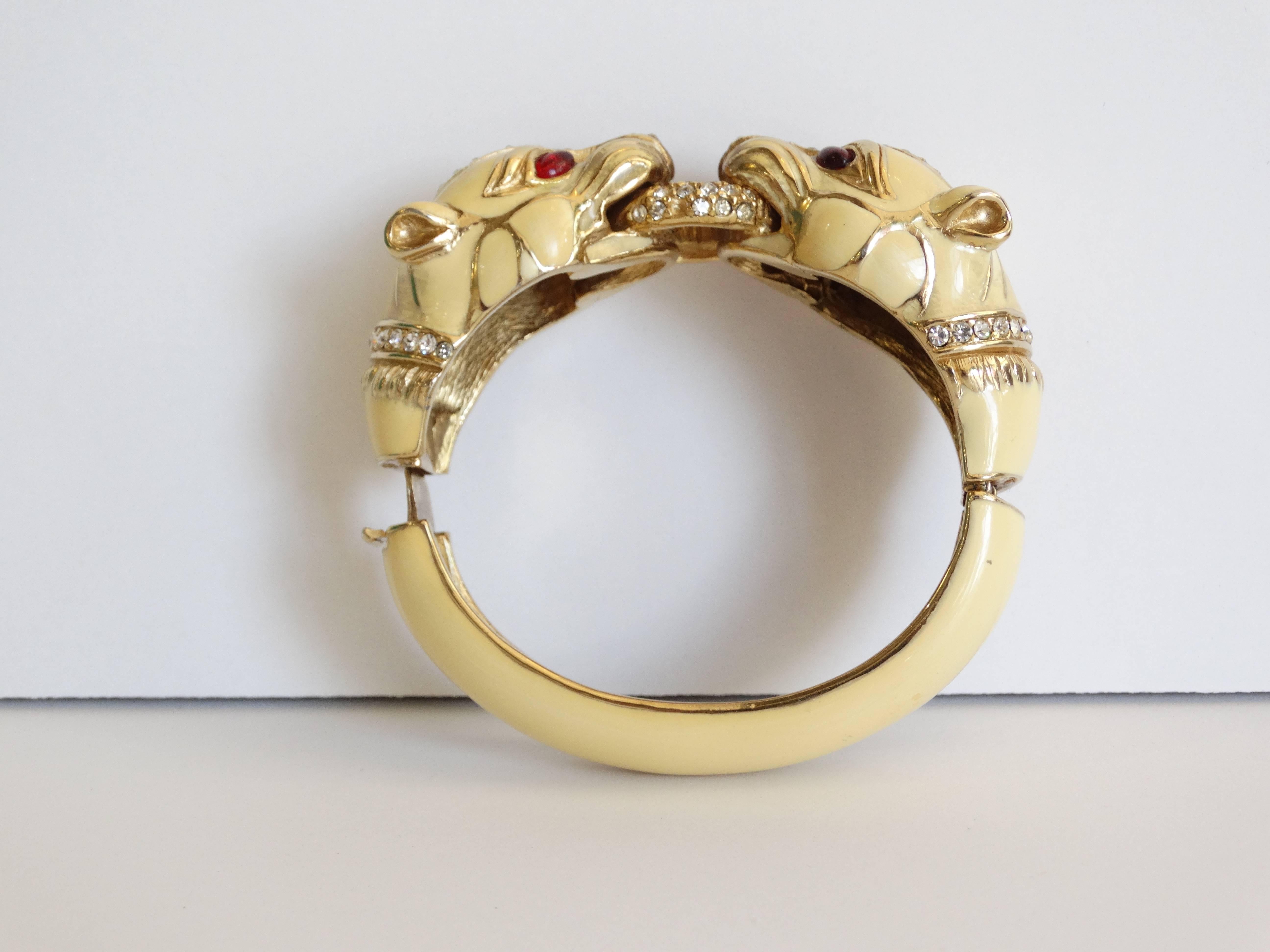 This fabulous Ciner enameled bracelet in cream is from the 1970s . It has double Panther heads that are encrusted with Swarovski Crystal jewels. Center Swarovski crystal o-ring,  Eyes are red cameo glass. Closure is a clamper style. The inside