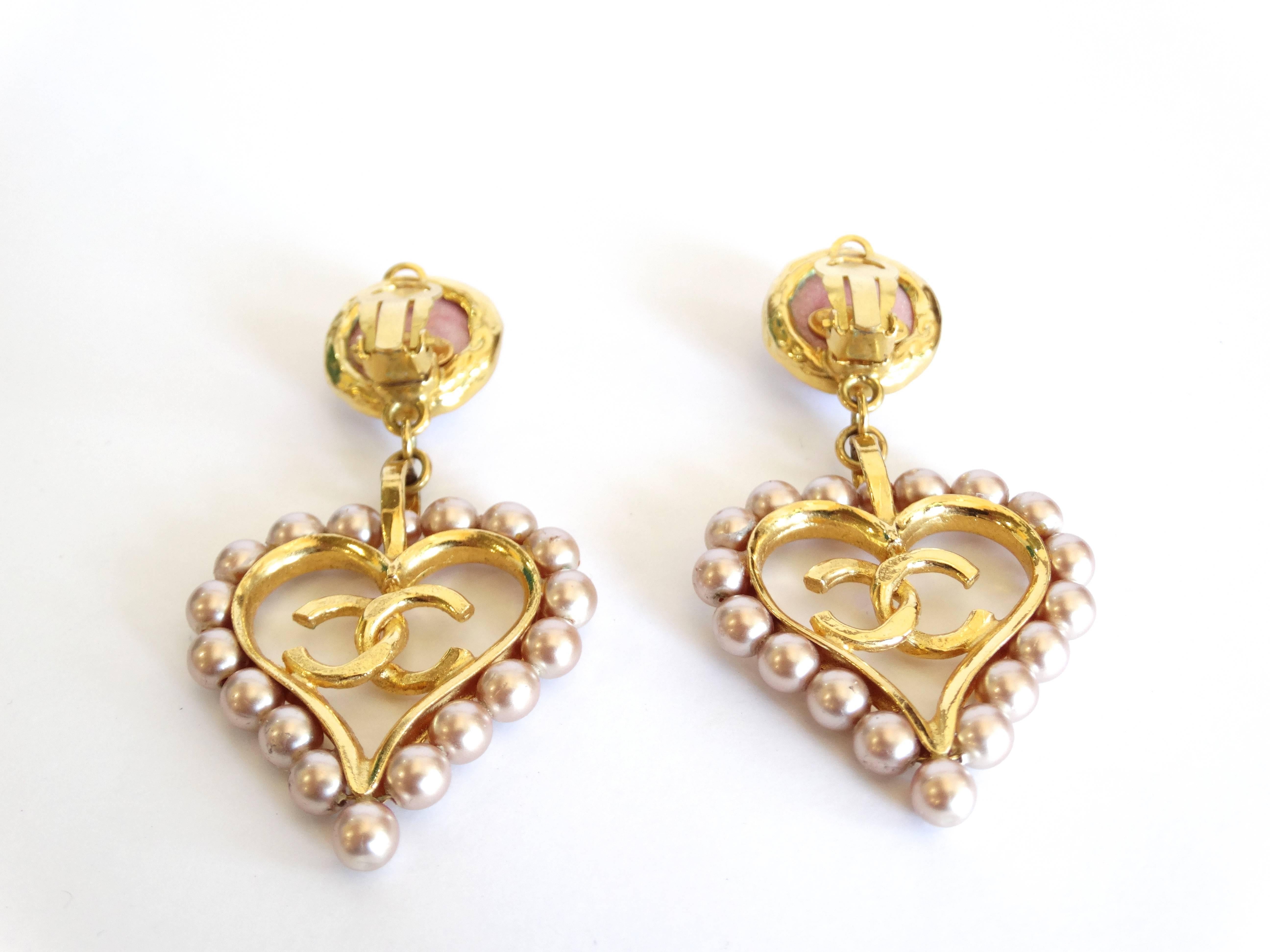 The cutest pair of 1990s Chanel heart drop earrings! Plated gold metal ; with center CC encased in heart- trimmed with pale rose faux pearls. Larger scale with Clip on backs. Comes with the original box. Made in France