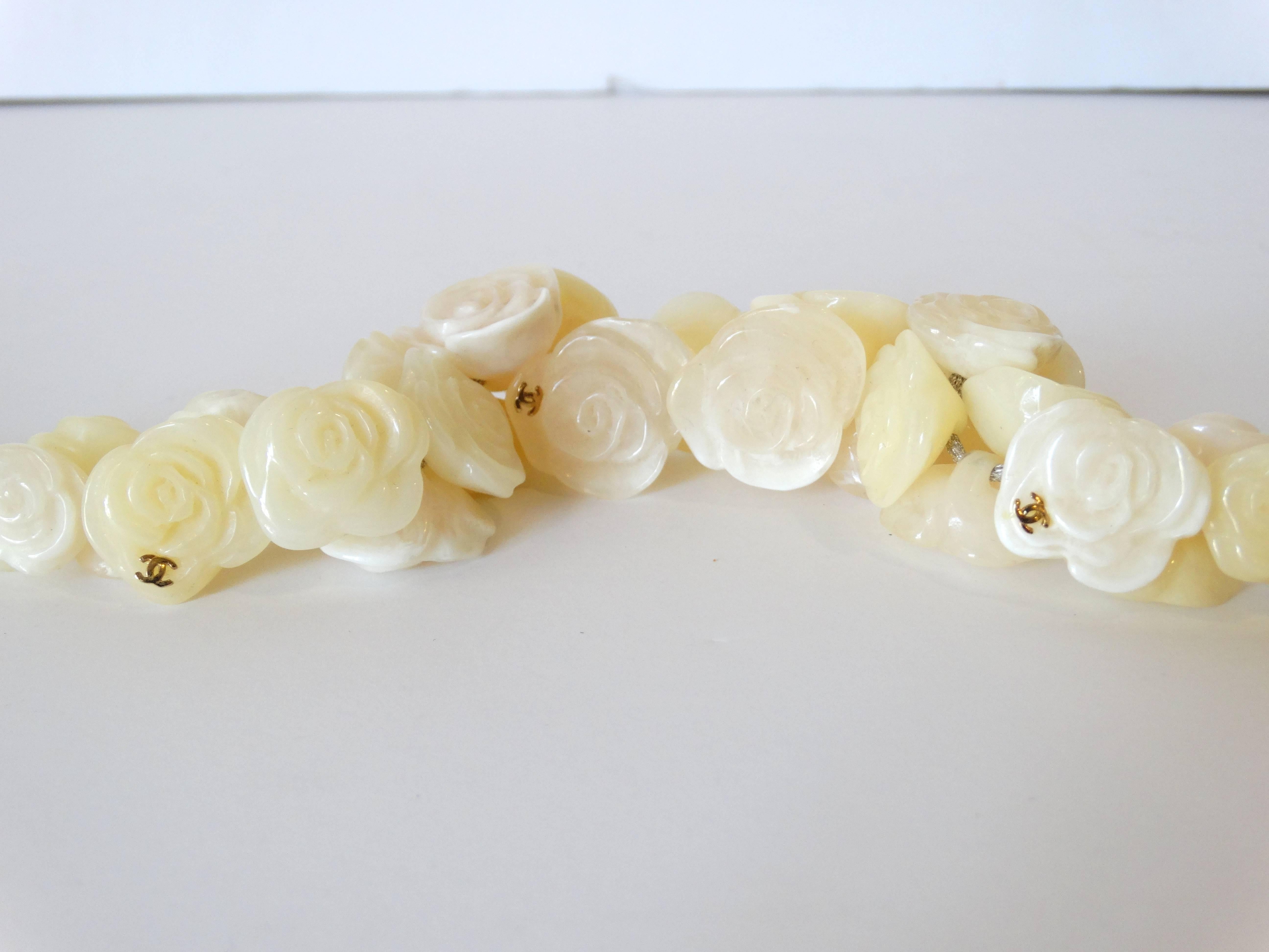 Gold-tone Chanel Camellia Floral choker necklace featuring ivory resin embellishments, metallic ribbon and self tie closure. Charm on one side of the ribbon is missing. Signed on the back of the petal charm. From the Spring 2002