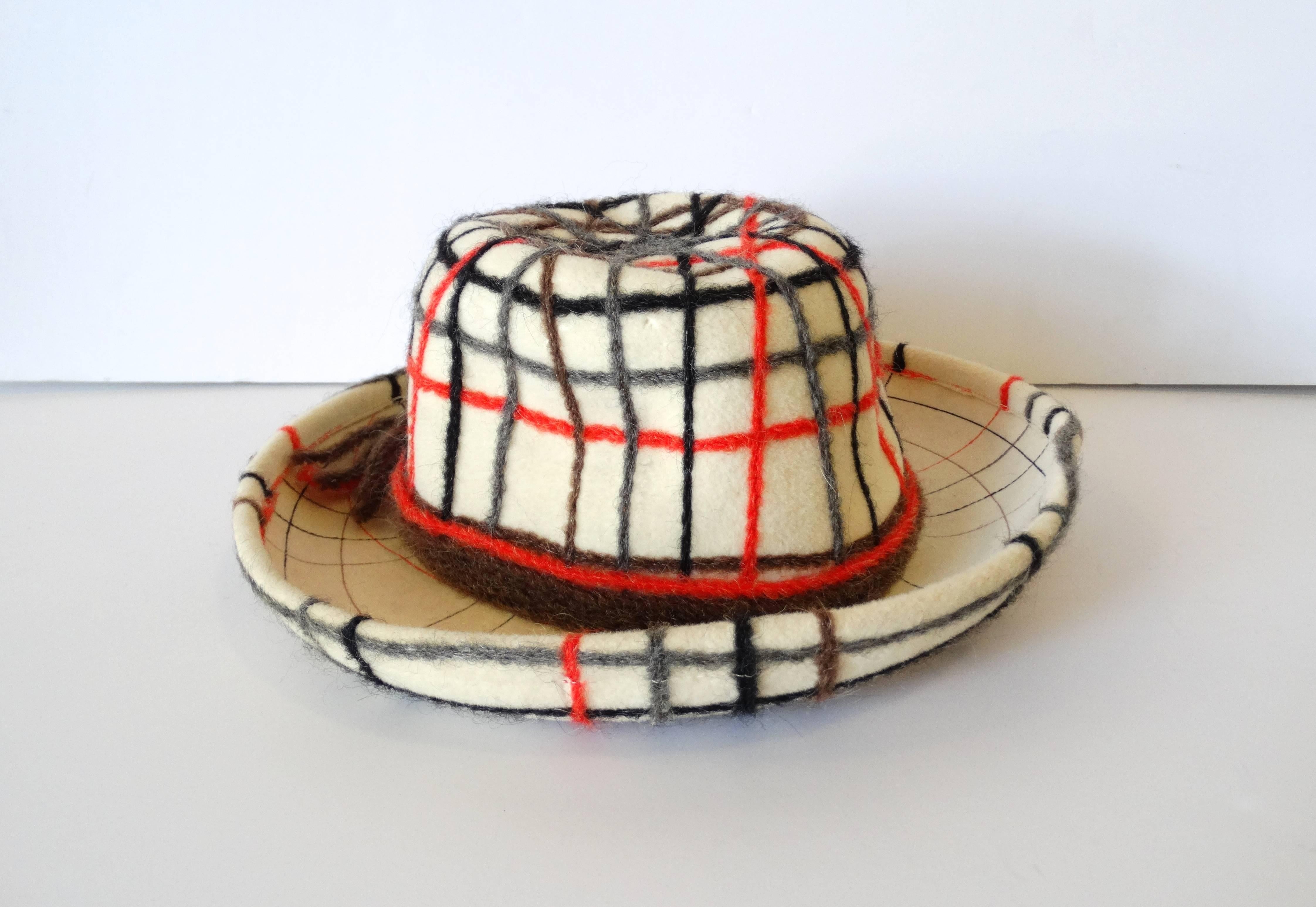 The classiest little plaid Yves Saint Laurent hat! very unique!! It is a cream colored wool accented with strands of grey, orange, black and brown wool yarn. It has a cute little pony tail of yarn at the back of the hat. Great piece for display, to