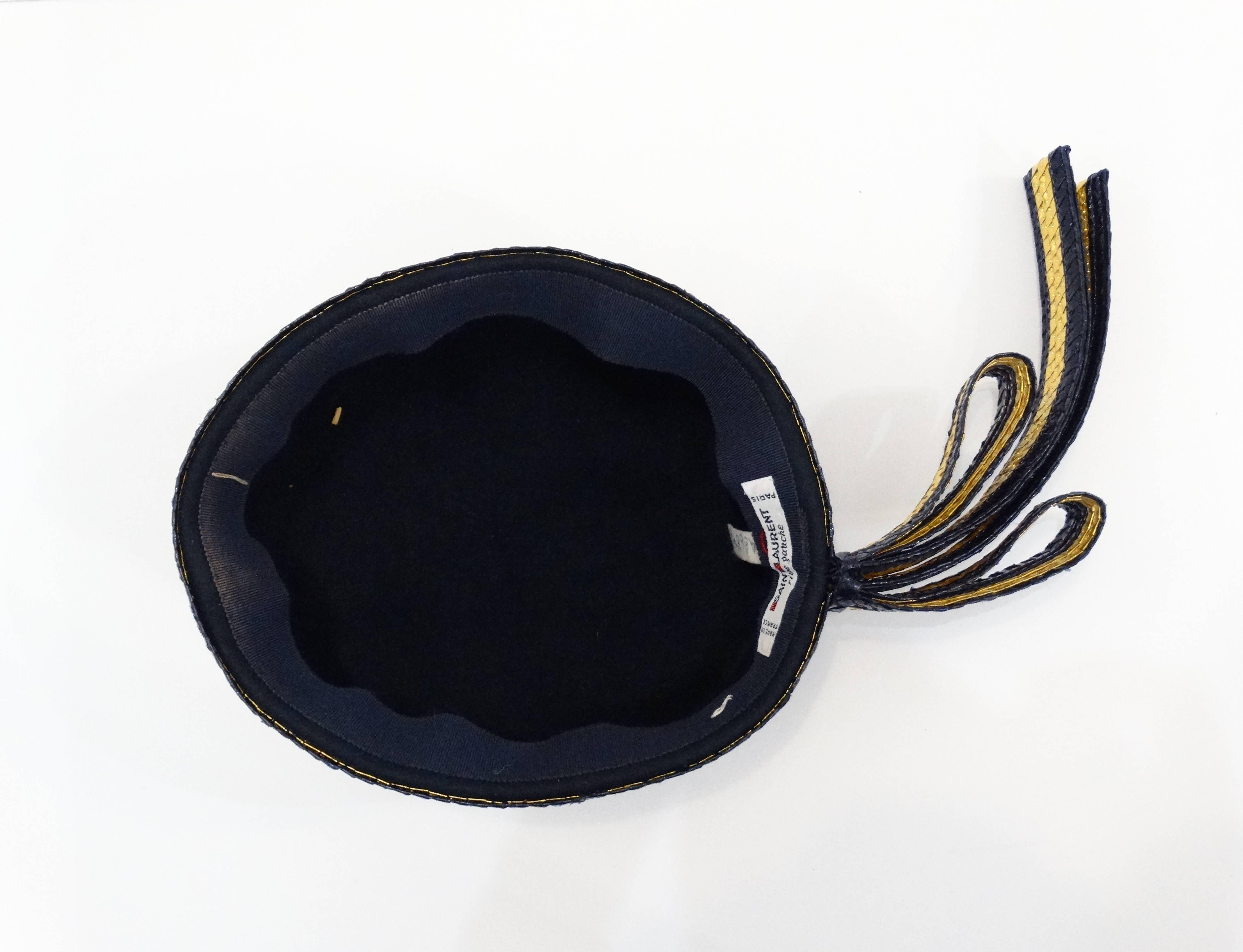 Channel the class of the 1960s with this Saint Laurent pillbox hat! Black felt with gold and black braided ribbon accents around the perimeter! Bow detail at the back adds some drama and flair!

Inside head band measures roughly 20 1/4 inches