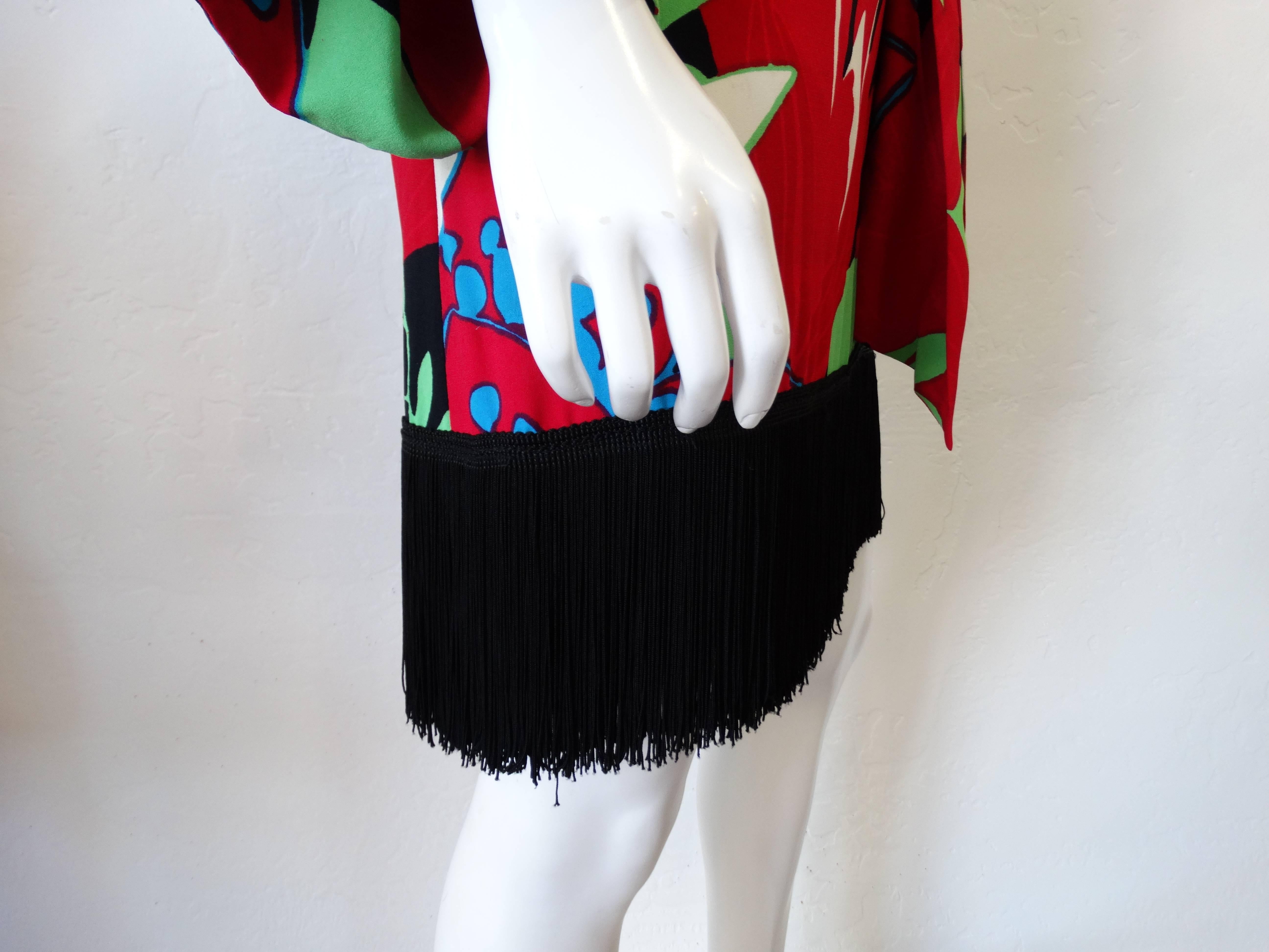 Incredible 1960s dress from Yves Saint Laurent's Rive Gauche line! Bold, bright multicolored floral print with matching tie at the waist. Classy shift silhouette with bell sleeves. Long black fringe trim along the hemline adds movement and drama.