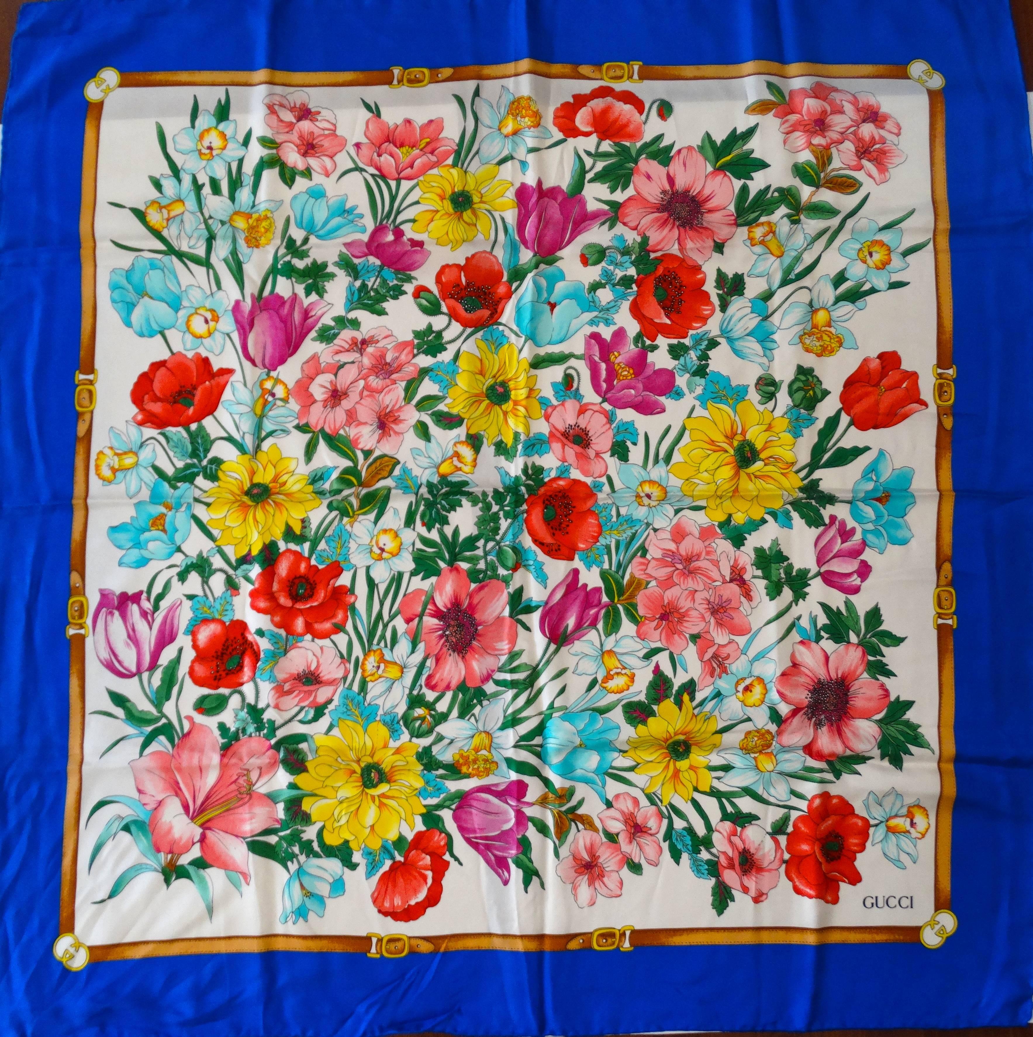 Beautiful 1970s Flora  Gucci scarf in brilliant multicolored floral print! Royal blue edges with insignias at the corners. Made of 100% silk.  35” by 35” Handrolled edges made in Italy 