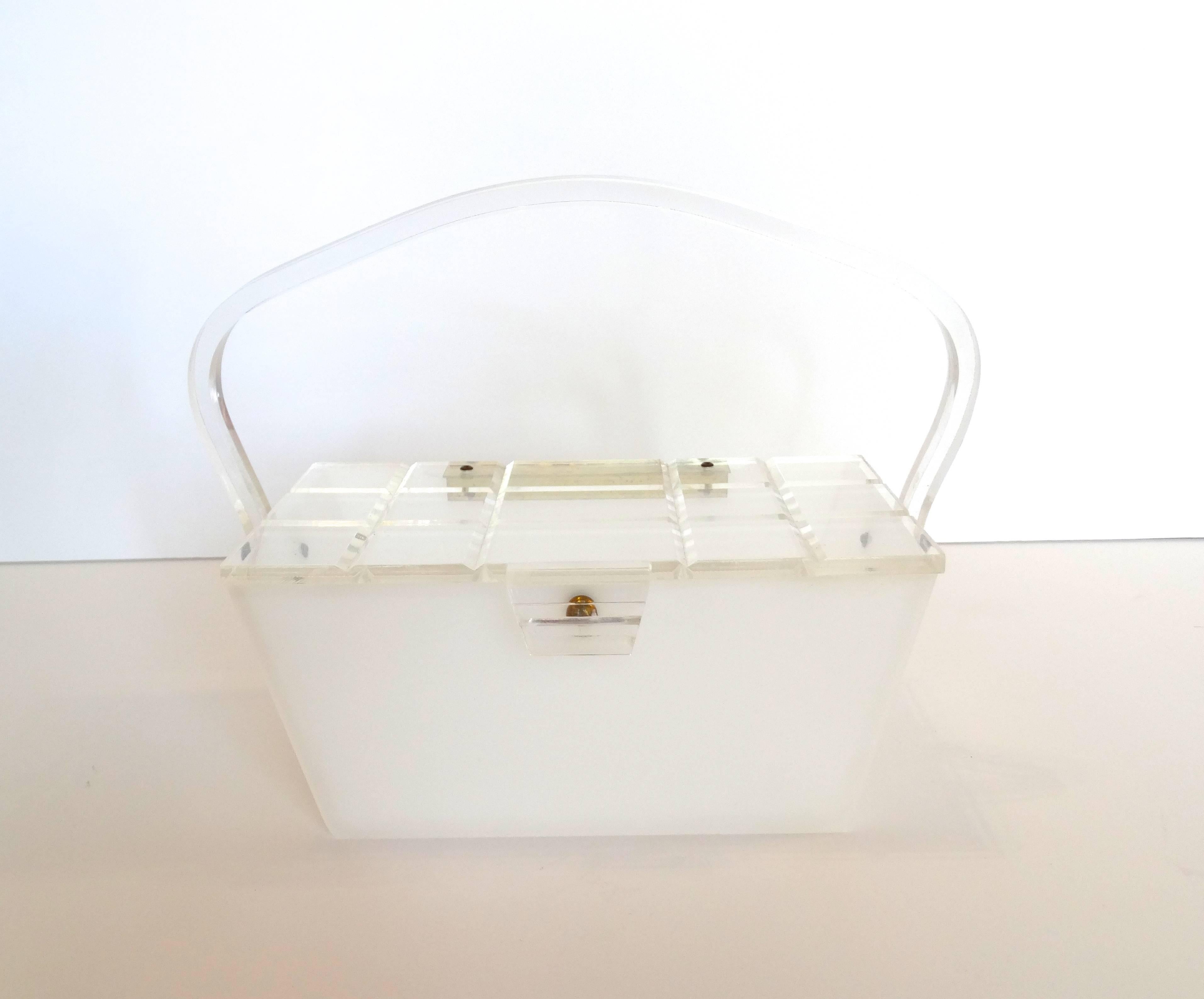 Fabulous geometric lucite purse from the 1960s. Milky, semi translucent lucite accented with gold hardware. Trapezoid shaped structure with top handle that can be folded over. Carved, grid like clear panel on the top, snaps into place. 


Width: