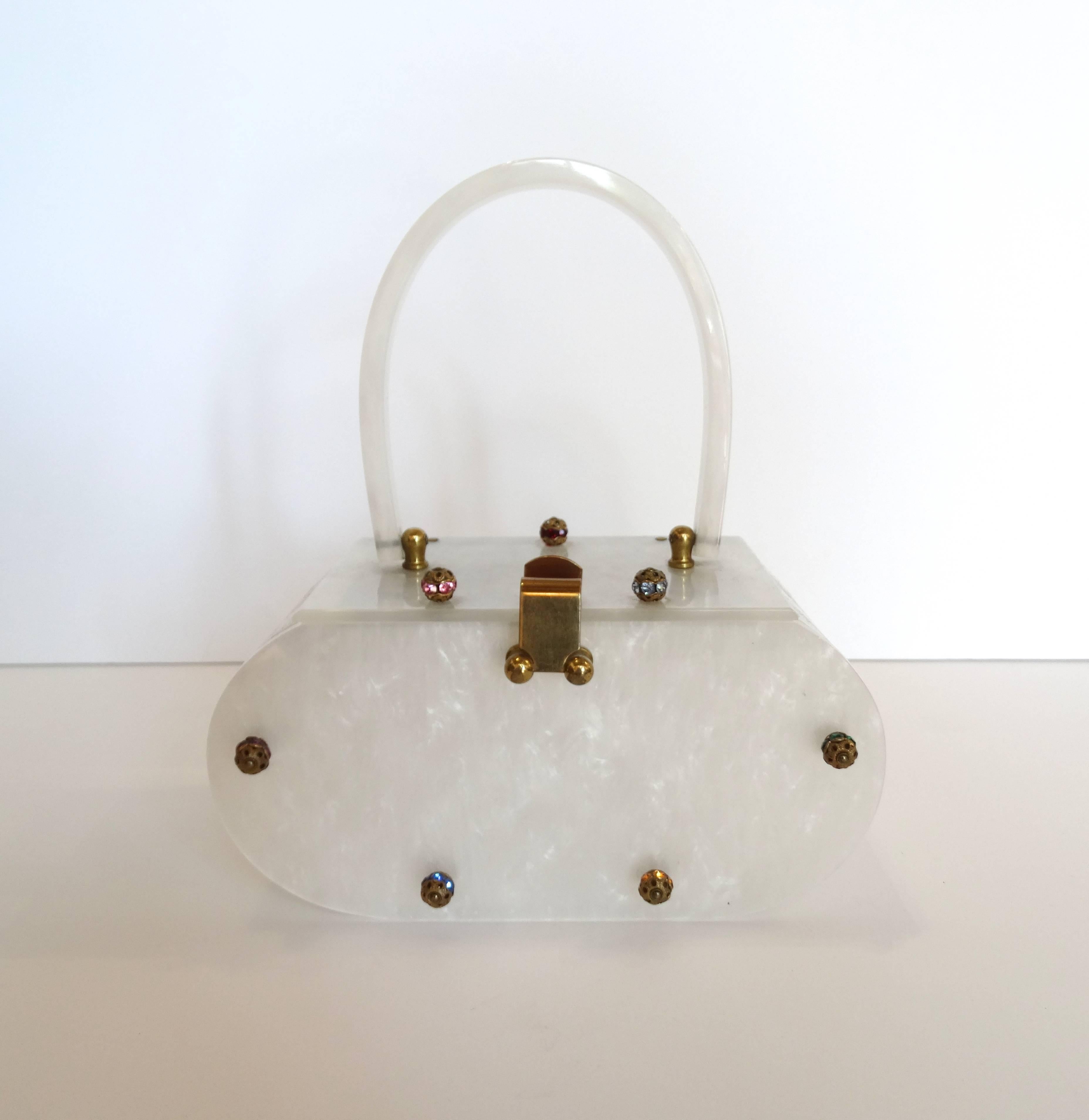 Fantastic 1960s Lucite evening bag! Accented with rhinestone orbs in an array of colors. Made of a milky, pearlescent lucite in a pill shaped structure. Stylish top handle folds over for easy storage. Hook closure snaps over the top. Bronze toned