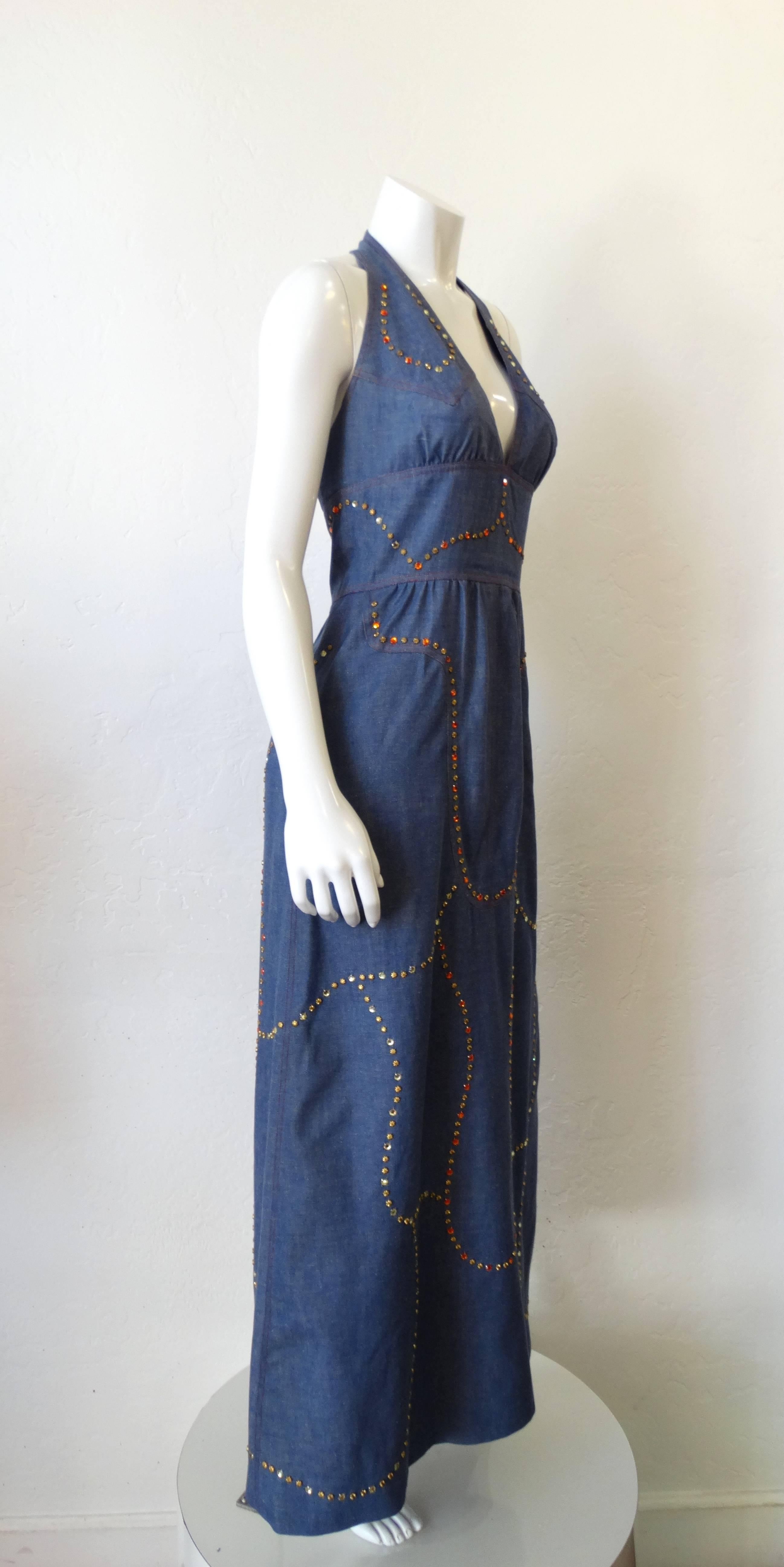 Live like a rhinestone cowgirl in our 1970s denim halter dress! True blue breathable cotton fabric accented with contrasted red stitching, gold studs and orange rhinestones. Sexy halter neckline and flattering empire waist with a maxi length skirt.