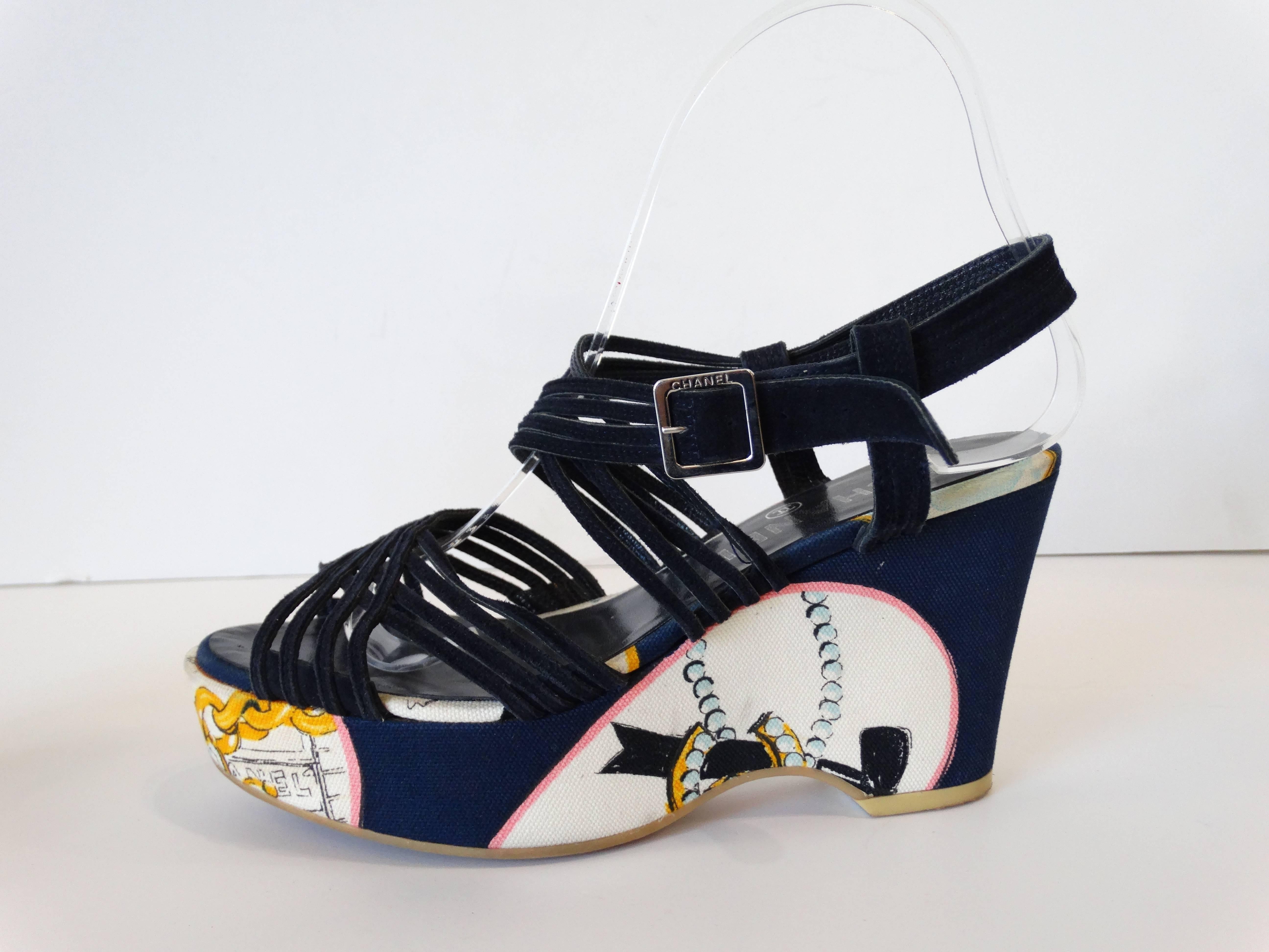 The perfect jet-setting wedges from iconic label Chanel! Deep midnight blue suede strappy construction with silver buckles at the ankle. Buckles signed with Chanel on the sides. Canvas print with Parisian motifs and classic Chanel chains, pearls and