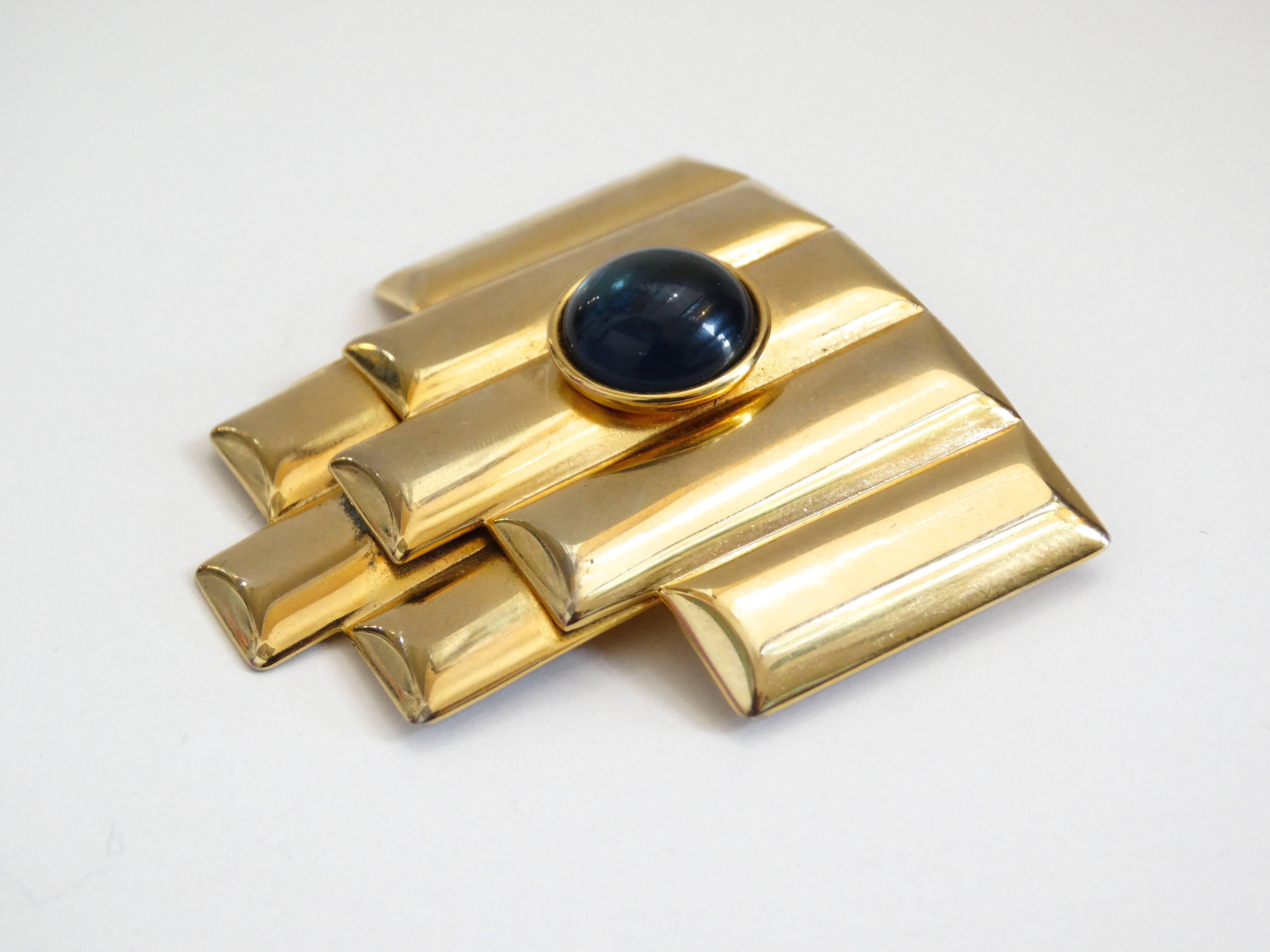 The perfect little gold brooch for all your evening looks from Balenciaga! This piece dates back to the 1980s, though it appears to be inspired by the art deco period of the 1920s. Gold toned metal in a layered, striped pattern, accented with a blue