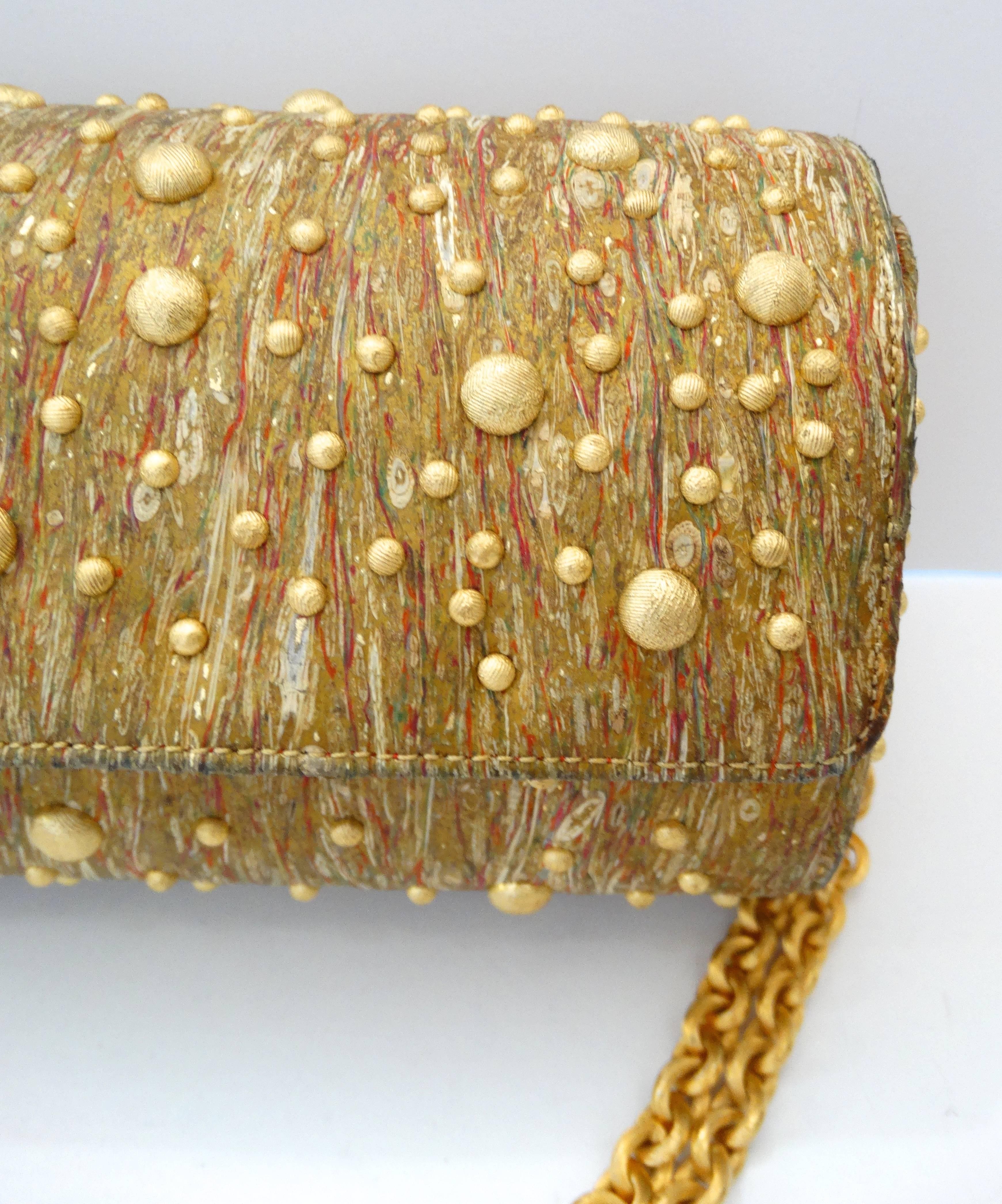 Amazing gold evening bag from the 1980s! Made of a gold toned fabric, accented with stripes of paint like textures. Covered in rounded gold metal studs throughout. Cylindrical shape, snaps into place with the top flap. Matching gold metal doubled up