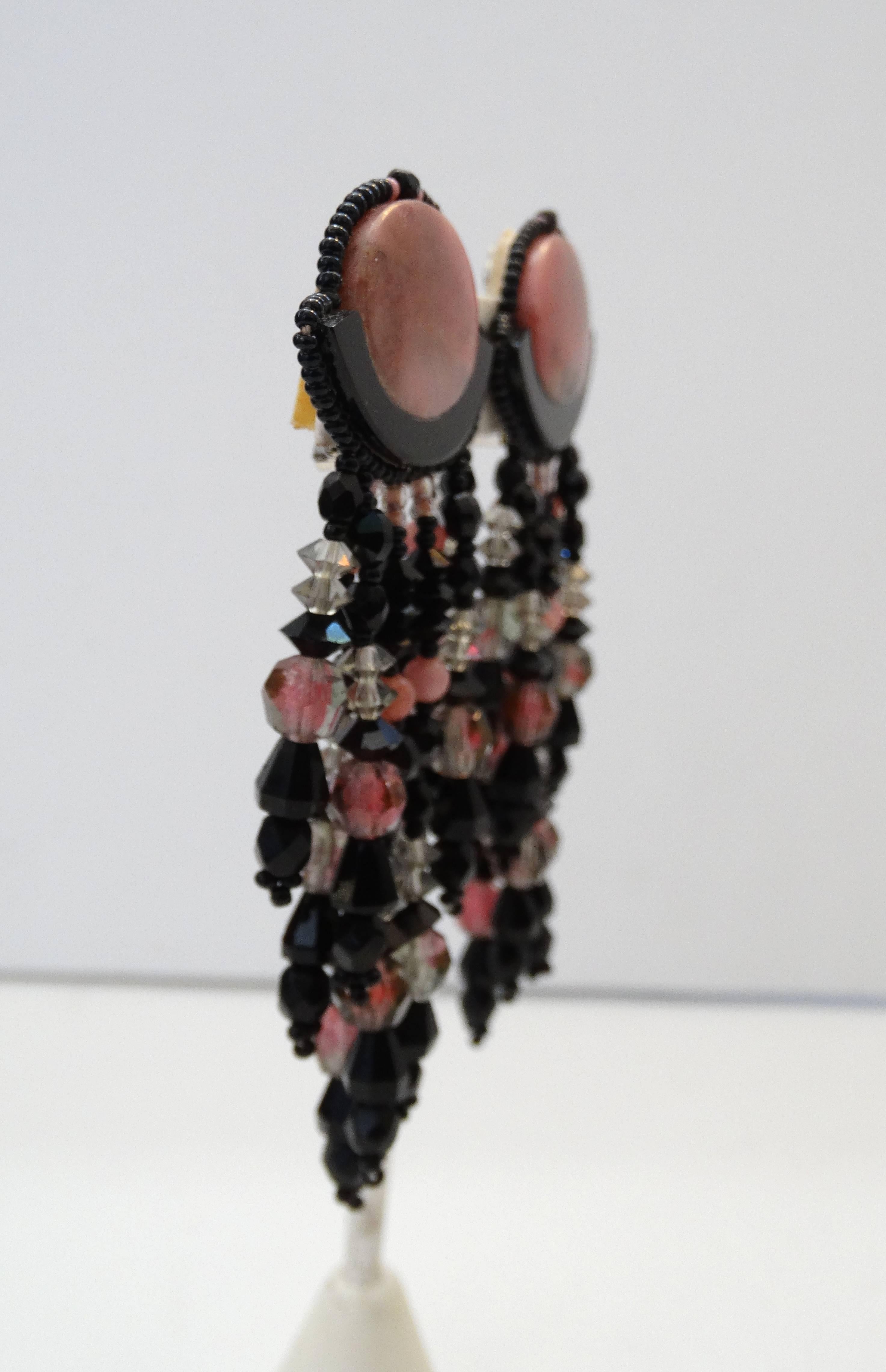 Rock a statement earring with our incredible beaded dangle earrings from the 1980s! Center charm made of a marbled pink stone and trimmed with stitched on black and pink beads. Strands of pink, clear and black beads suspended from the center charm.