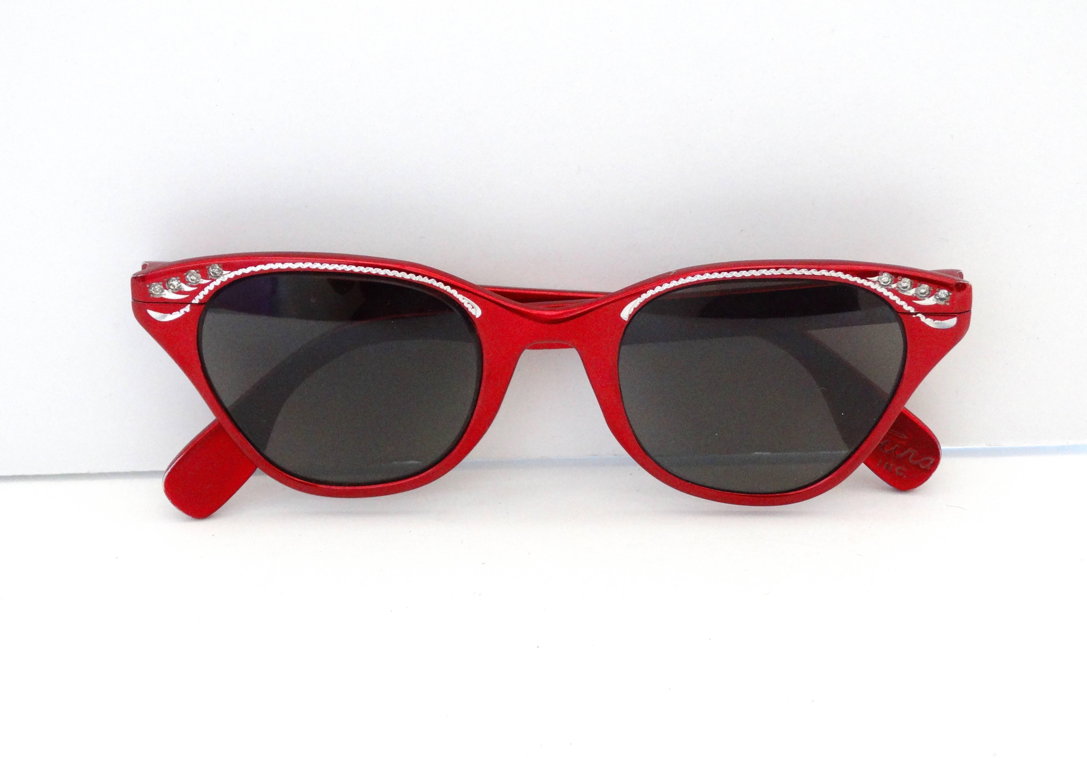 The perfect sunglasses for riding with the top down- head scarf and all! Classic metallic red cat eye sunglasses from iconic vintage eyewear designer, Tura. Accented with silver details and rhinestones around the top rims. Dark grey tinted lenses.