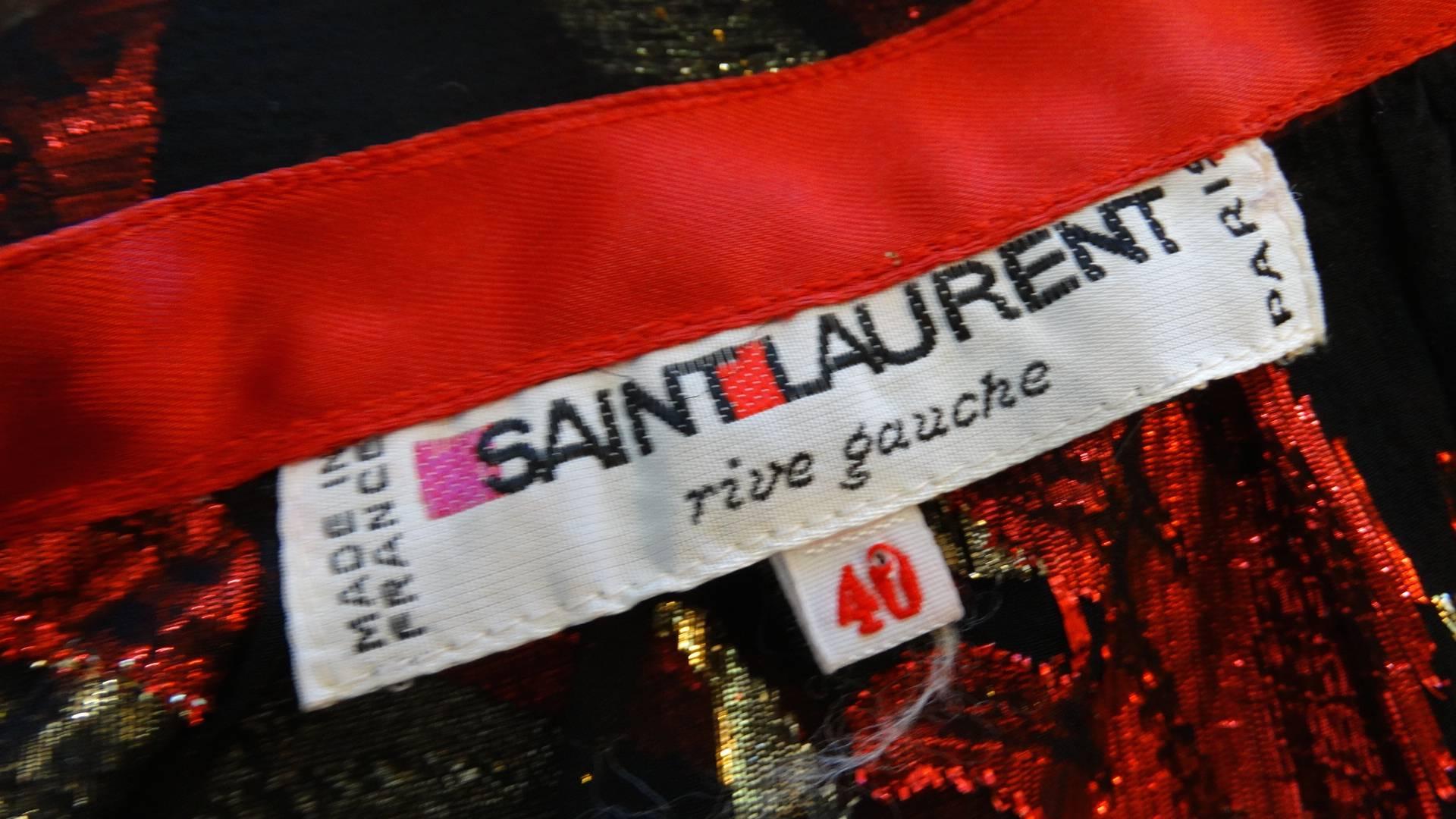 Gorgeous 1980s Saint Laurent Rive Gauche printed sheer skirt! Black sheer chiffon fabric with metallic red and gold flame-like pattern woven throughout. Red ribbon trim with excess at the waist, ties perfectly into a bow. Long, sexy slit up the left