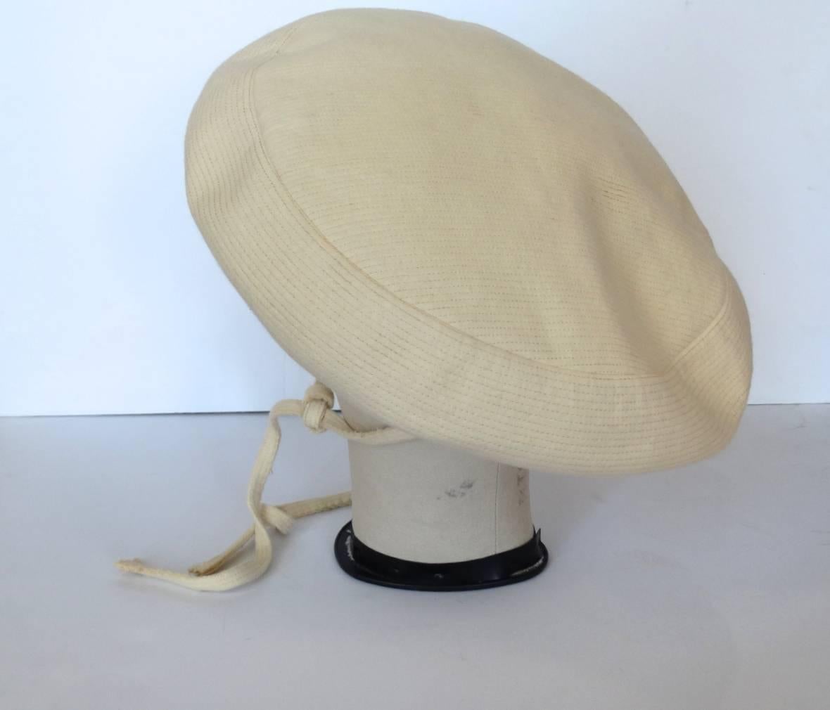This vintage Yves Saint Laurent cream wool tam style hat, circa late 1960's, is too chic to ignore. This hat features a cream wool exterior along with cream pin stripe top stitch detail, Wide flat top/brim, and Two long wool ties with fringed ends