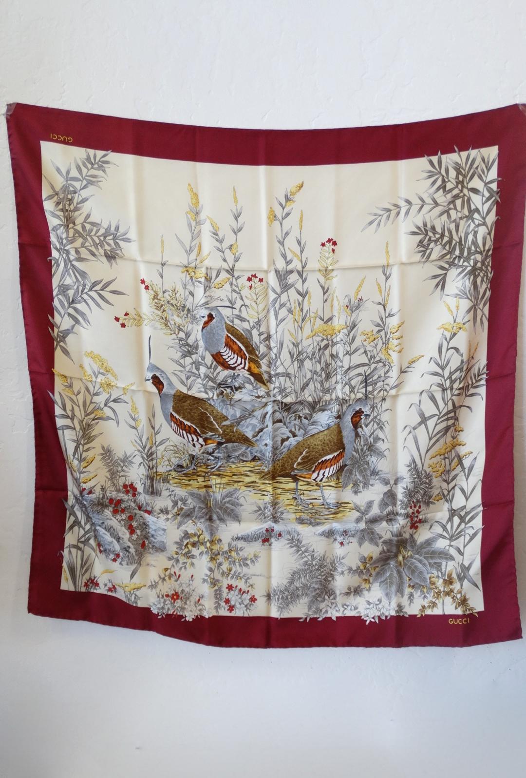 The perfect piece for the holiday season- Aviary 1980s Gucci silk scarf! Printed with an earthy toned scene of several Quail birds standing in the desert brush. Deep red border along the perimeter of the scarf. GUCCI printed in the gold on the