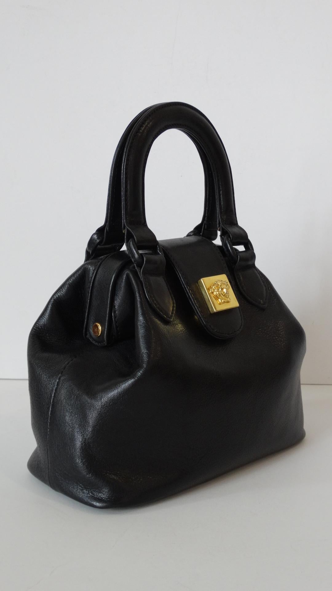 Channel your inner 90s chick with our adorable Gianni Versace black leather top handle bag! Doctor's bag construction with circular double handles. Made of a quality black leather with matching leather blacked-out hardware. Features Versace's