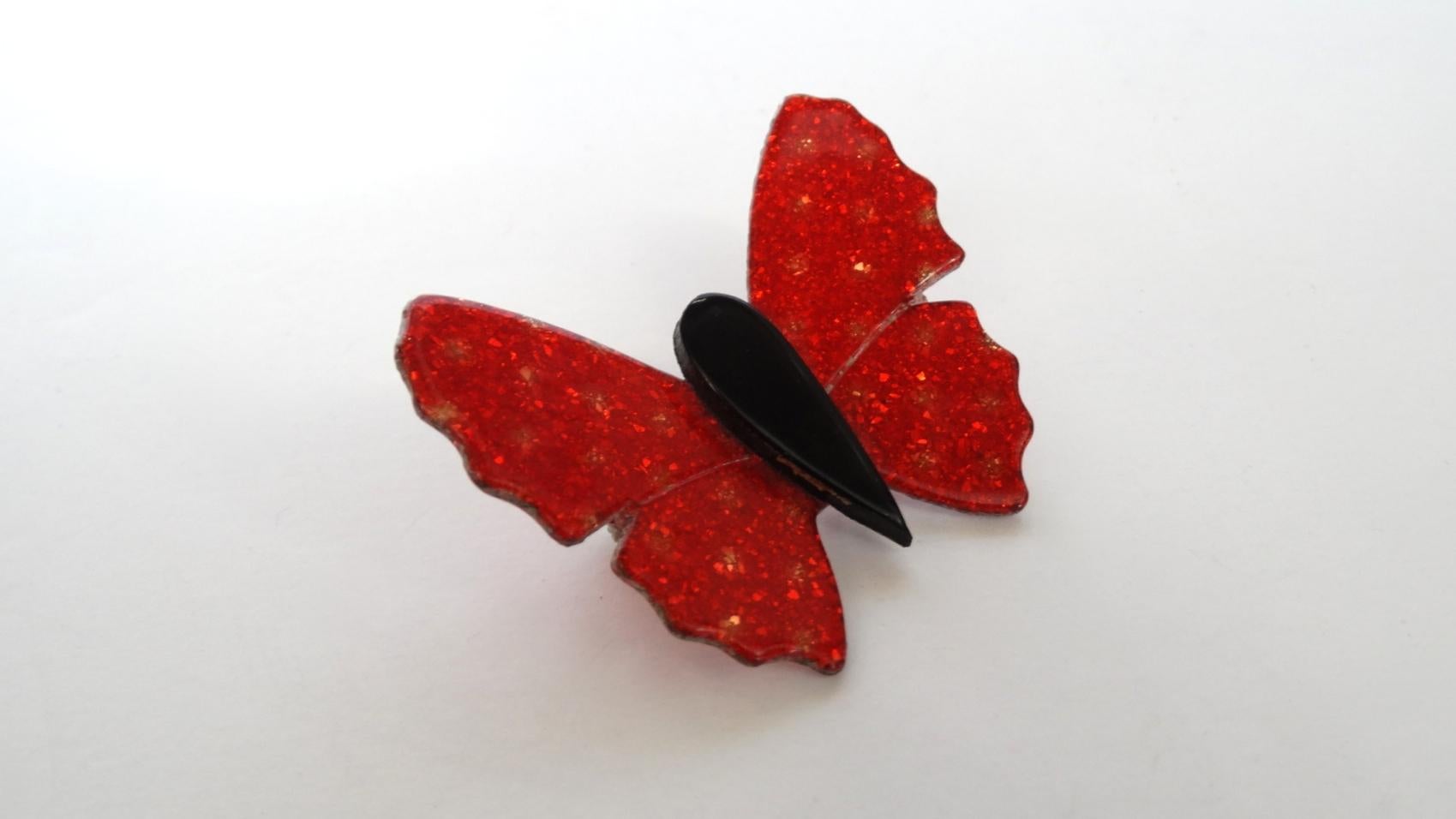 Brooches Are The New Hot Accessory This Season And We've Got You Covered! Circa 1970's, this Lea Stein butterfly brooch features a glitter flake effect in vibrant red and accented with subtle gold dots. A black tear drop shaped body adds dimension