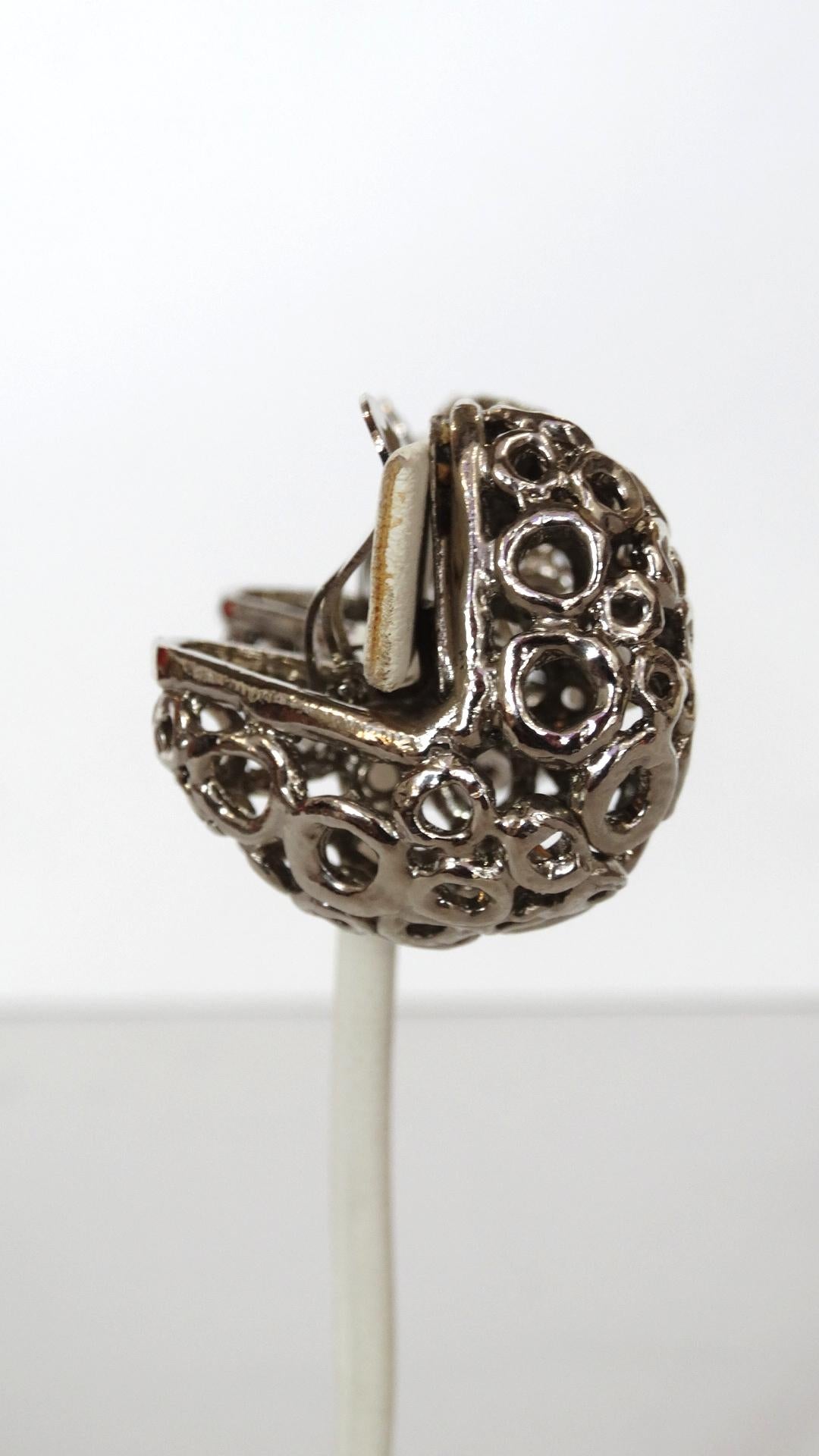 If You're In Need Of Statement Earrings, They've Arrived! Circa 1980s, these silver plated earrings feature a 3-D cage structure that curves in a V shape behind the ear. Decorated with differing sized circles and includes clip-on closures. Signed